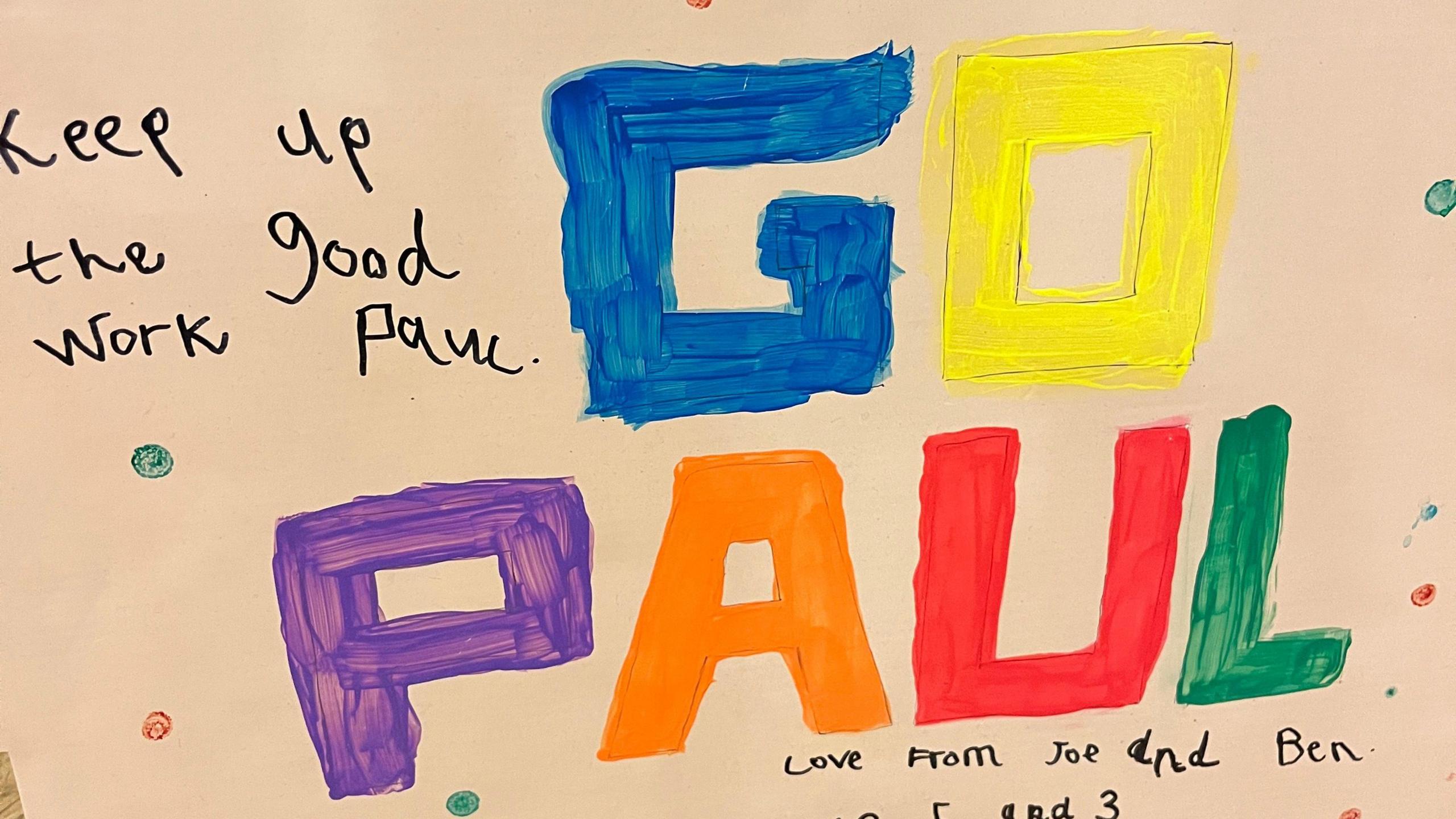 A sign made by children that reads "Keep up the good work Paul. Go Paul", in multicolour letters