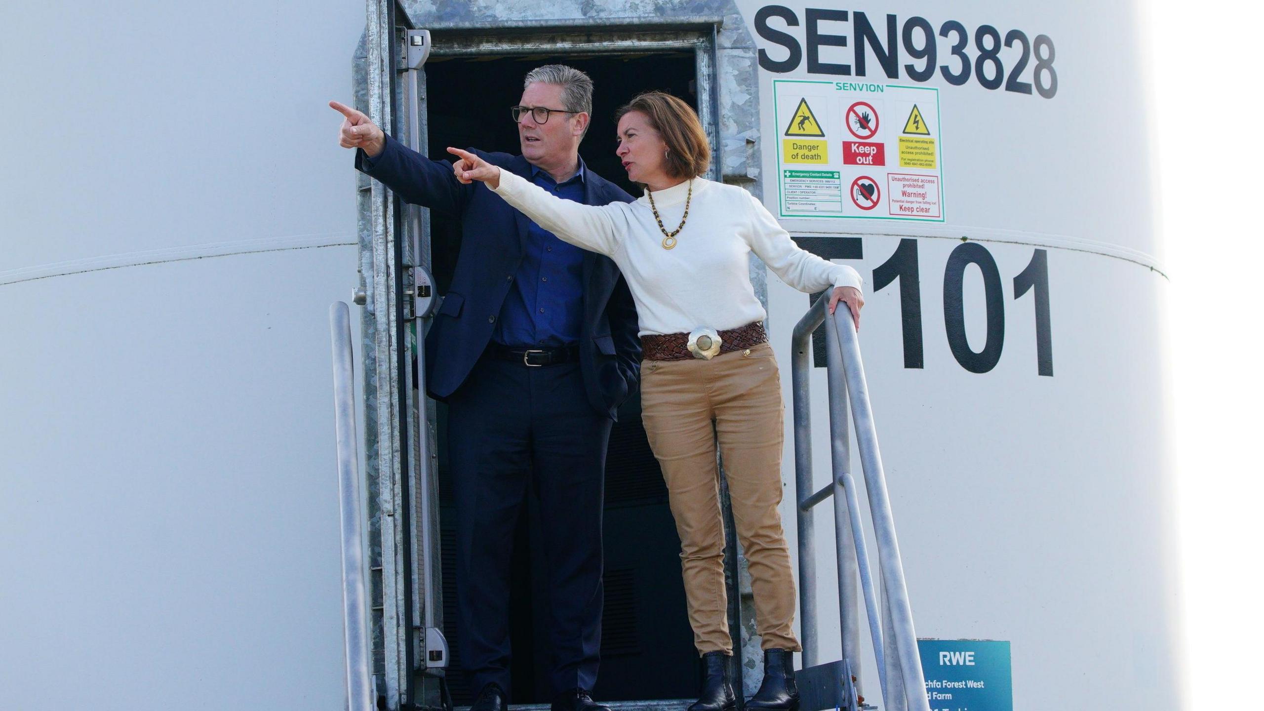 Sir Keir Starmer and Eluned Morgan stood at the door of a wind turbine, both pointing in the same direction.