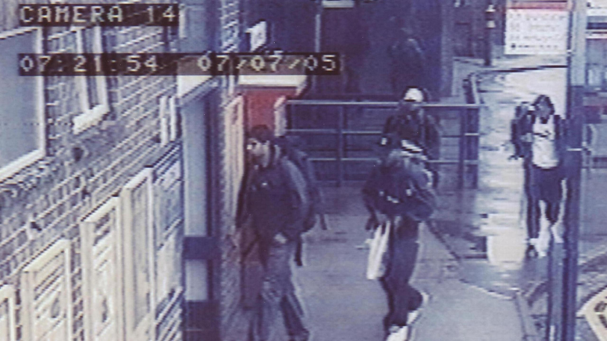 A grainy CCTV image of four men dressed mainly in dark clothing walking towards a door entrance. Two of the men are wearing caps and some can be seen carrying backpacks.