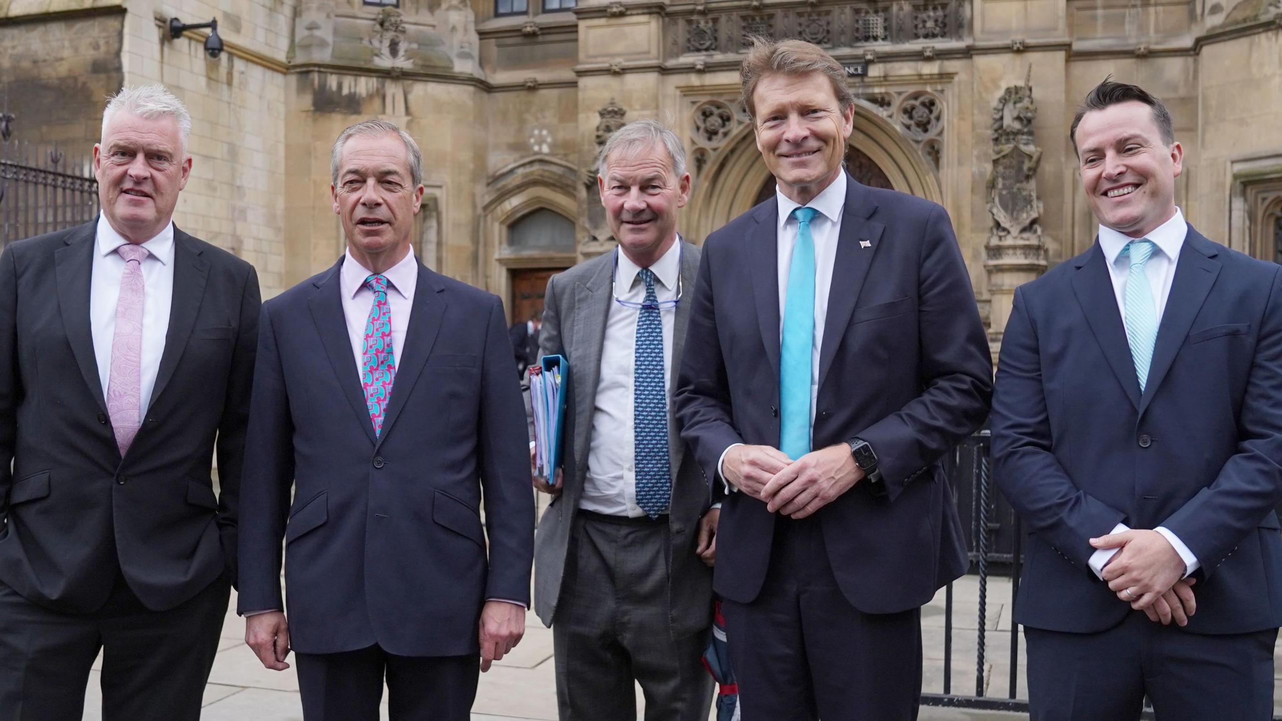 Reform UK MPs Lee Anderson, Nigel Farage, Rupert Lowe, Richard Tice and James McMurdock arrive at the House of Commons. They are in a row wearing suits and ties of various hues.