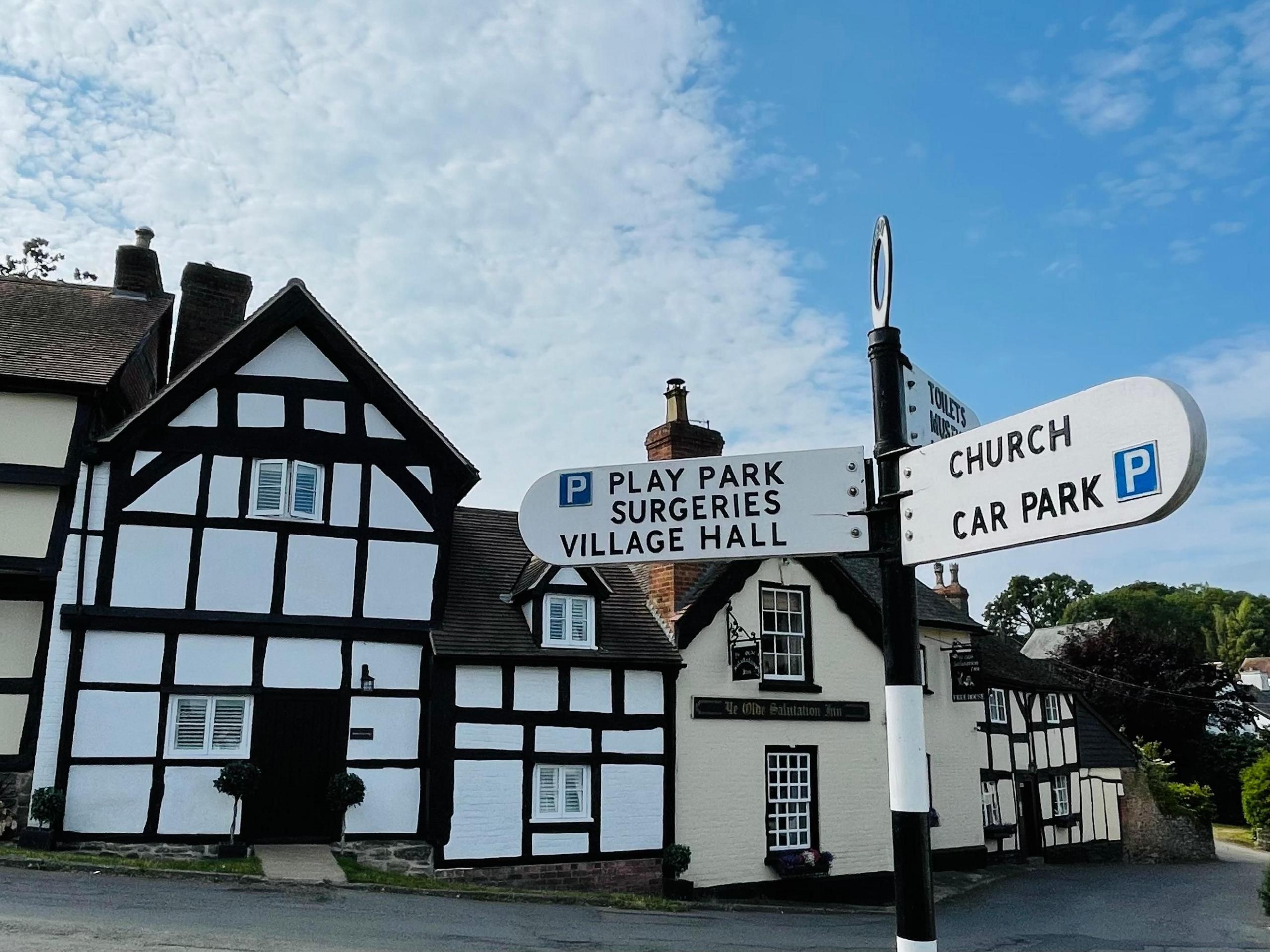 Street scene featuring a black-and-white timbered house, Ye Olde Salutation Inn and a cream-and-white timbered house, with a wooden signpost in the foreground.