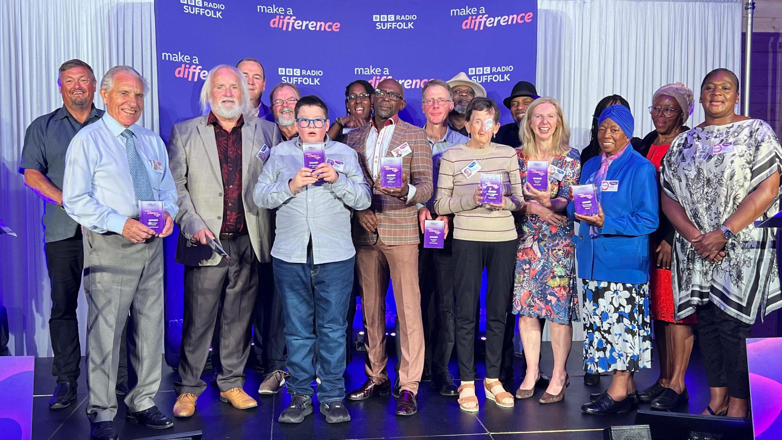 A selection of people on a stage, holding awards trophies