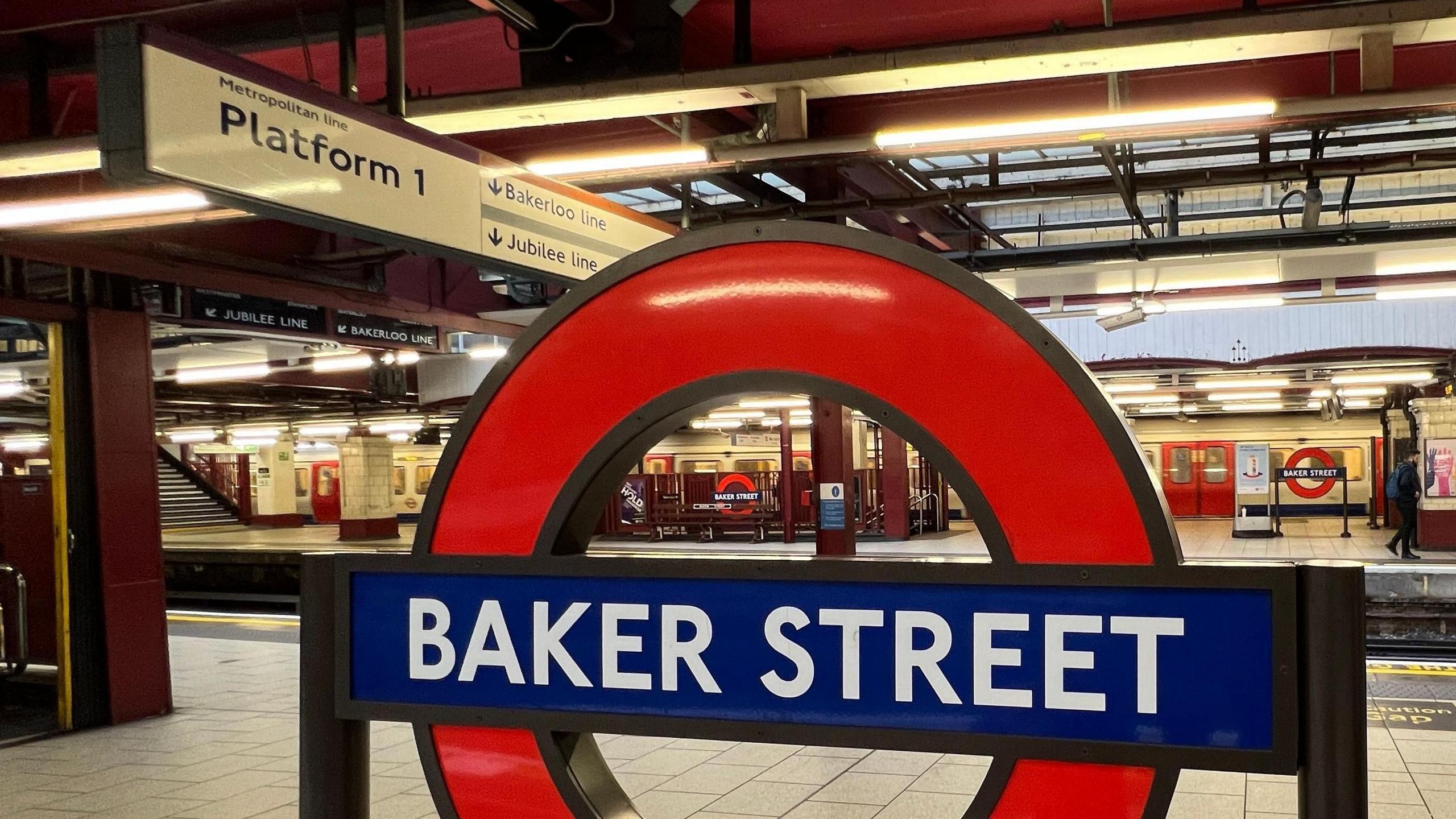 Image of a red and blue roundel sign for Baker Street, with the white tiled platform behind