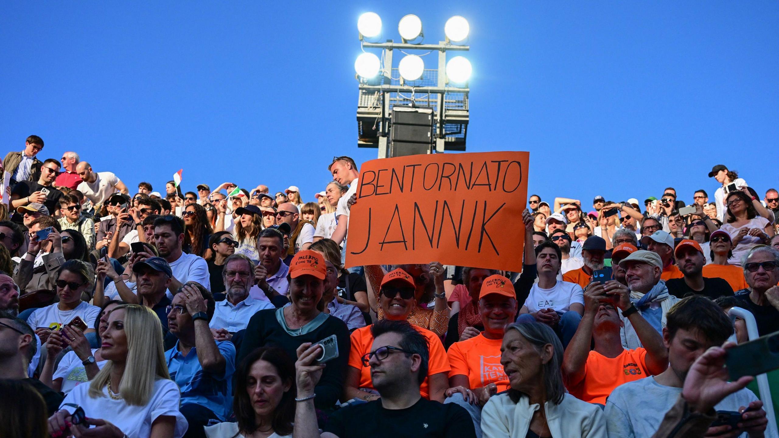 Fans hold up a sign saying 'Welcome back Jannik' during Sinner's victory