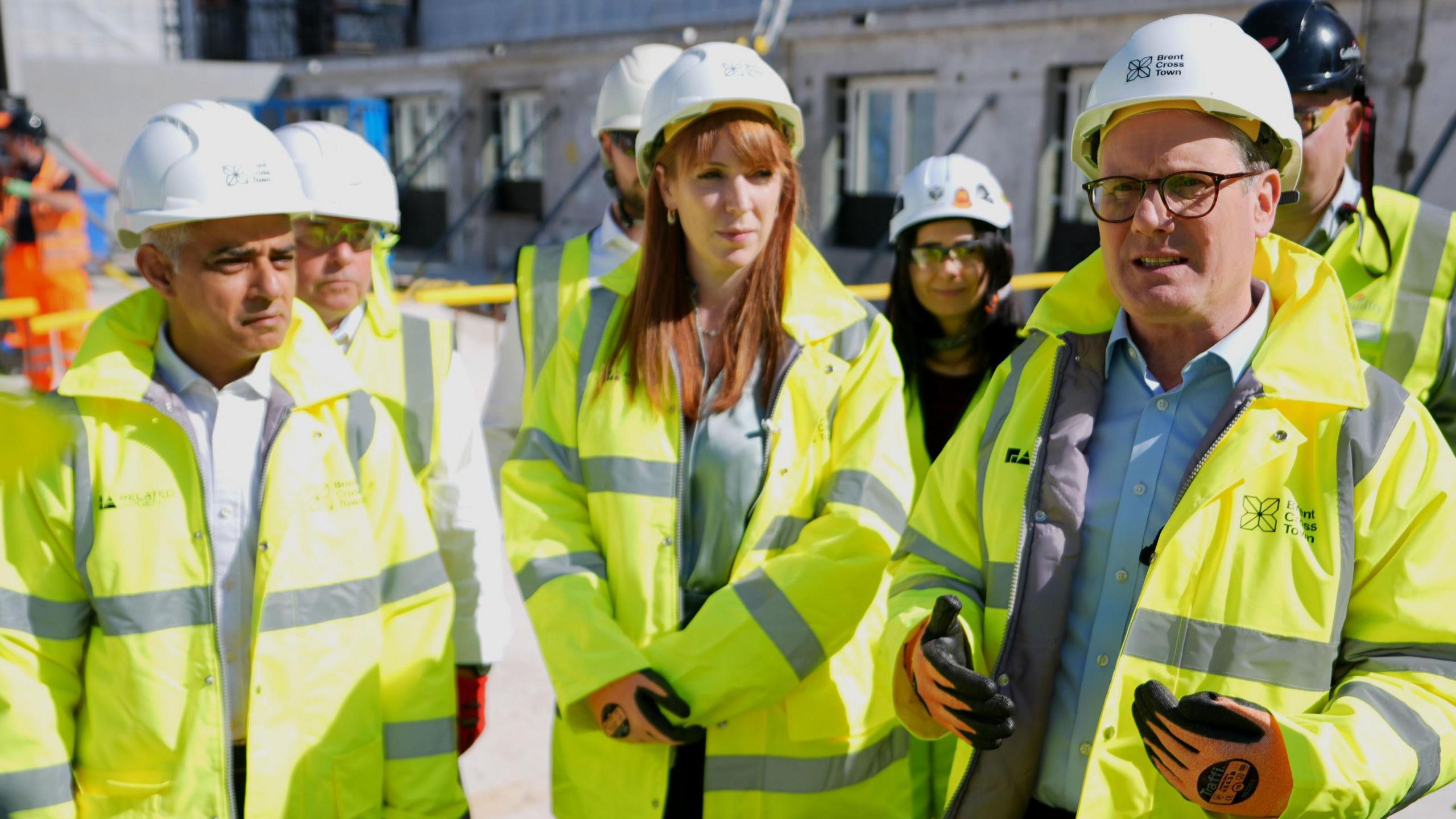 Mayor of London Sadiq Khan stands next to housing secretary Angela Rayner and prime minister Keir Starmer at a building site - all three are wearing high-viz jackets, hard hats, goggles and work gloves. 