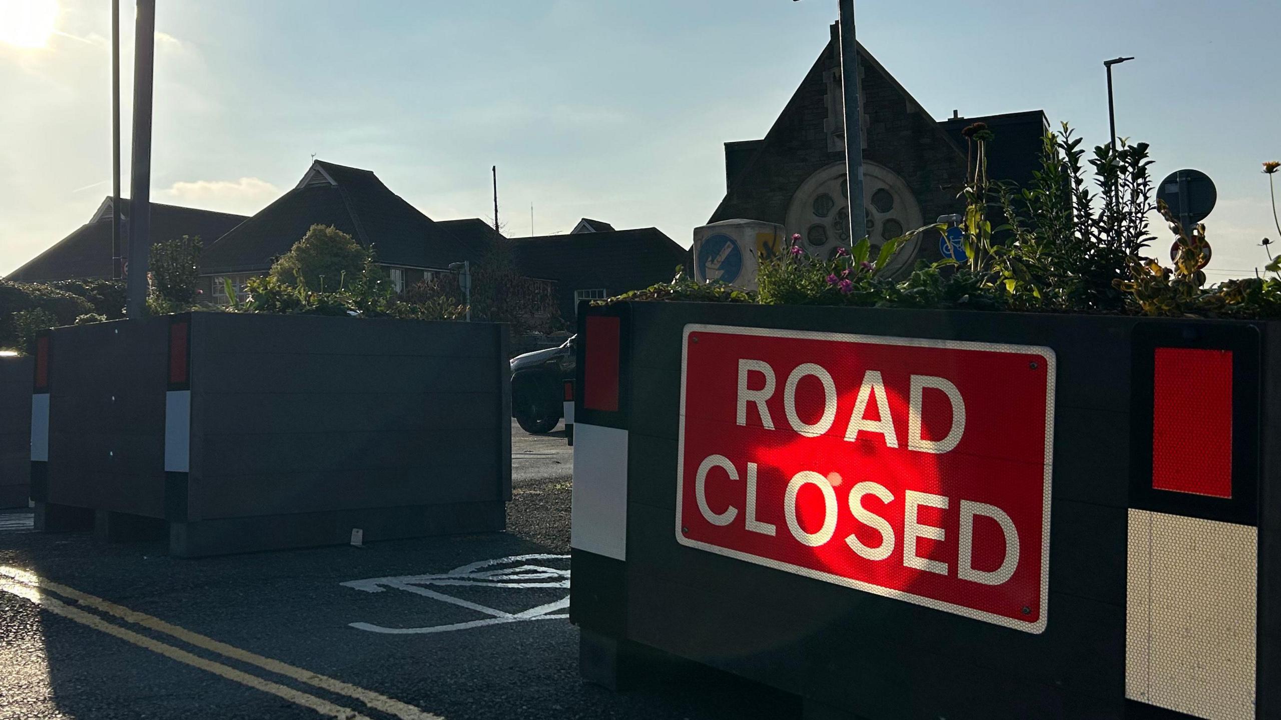 A road in Bristol has planters at the end of it to close it off to some traffic and a red and white "road closed" sign placed on it. 