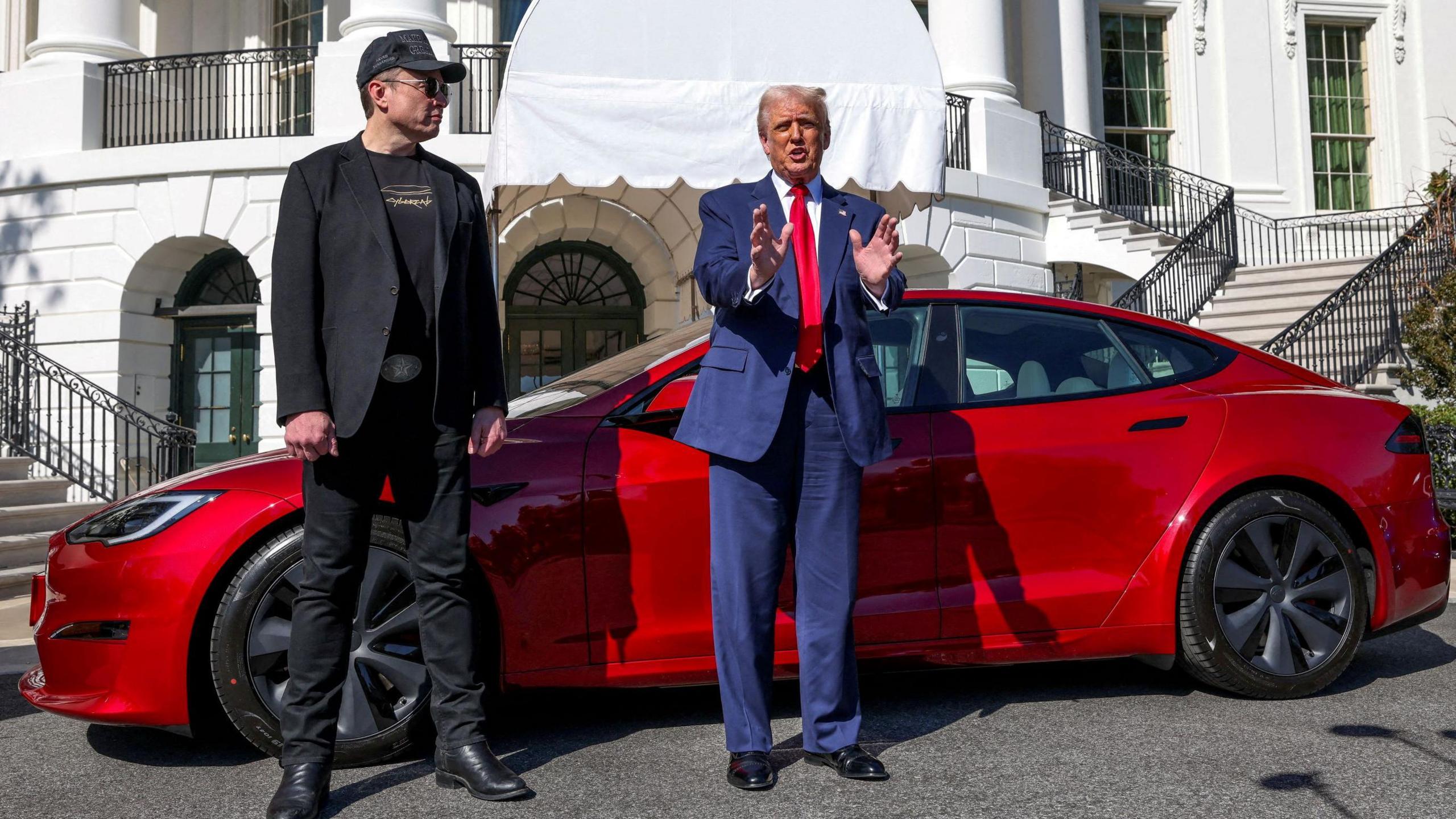 Elon Musk and Donald Trump stand in front of a red Tesla car which is parked in front of the White House in Washington D.C, United States.