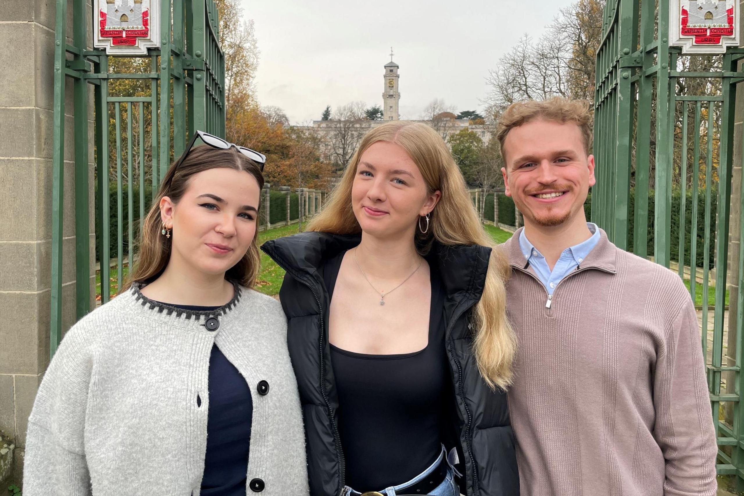 Students Lily-Rose Marsden, Charlie Blair and Max Hegarty standing in front of the gates outside Highfields Park in Nottingham with a university building visible in the distance