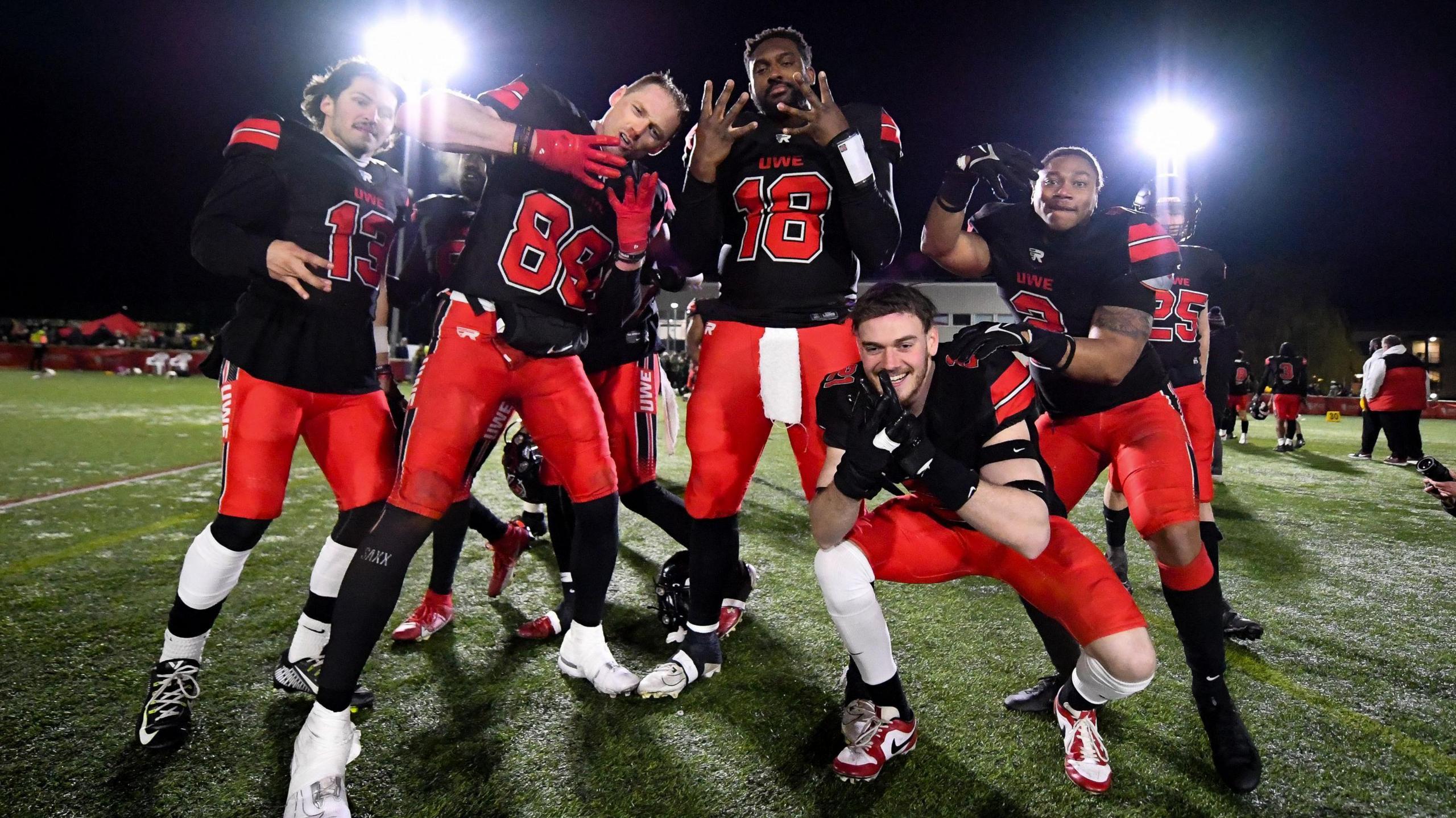 A group of American football players from UWE Bristol pose for the camera after beating Nottingham Gold. They are in the UWE kit of red trousers and black jerseys.