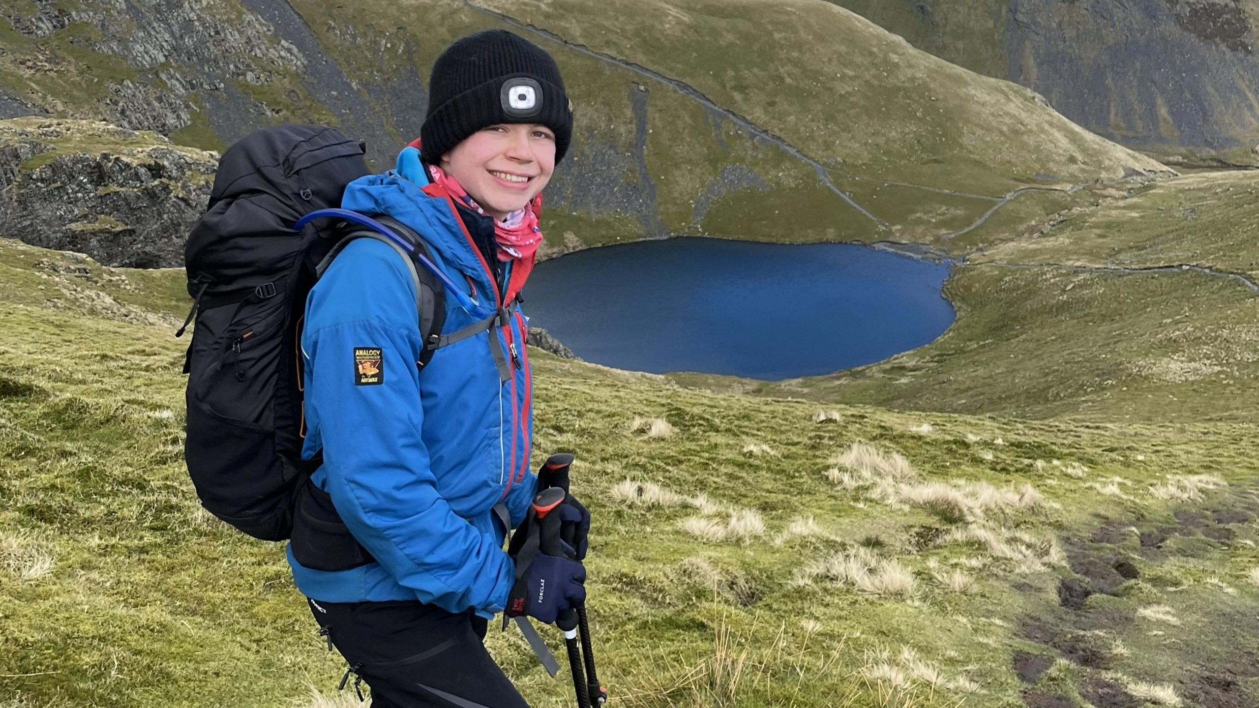 A teenage boy hiking on a hill with a lake in the background.