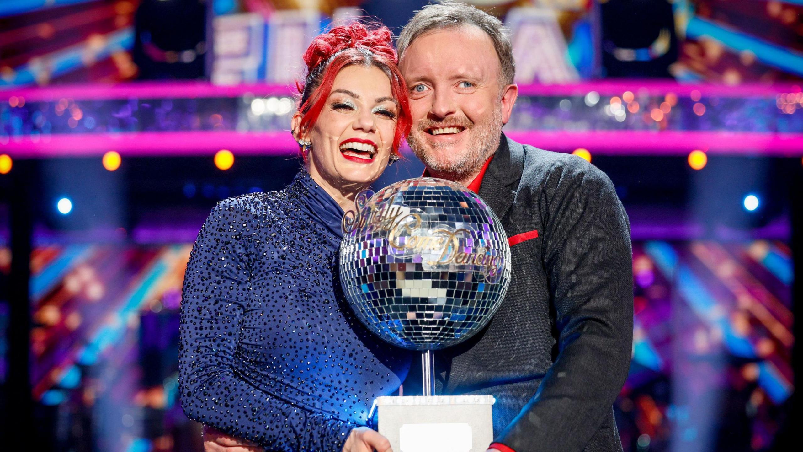 Dianne Buswell and Chris McCausland standing together, smiling and holding the glitterball trophy after winning the Strictly Come Dancing final.