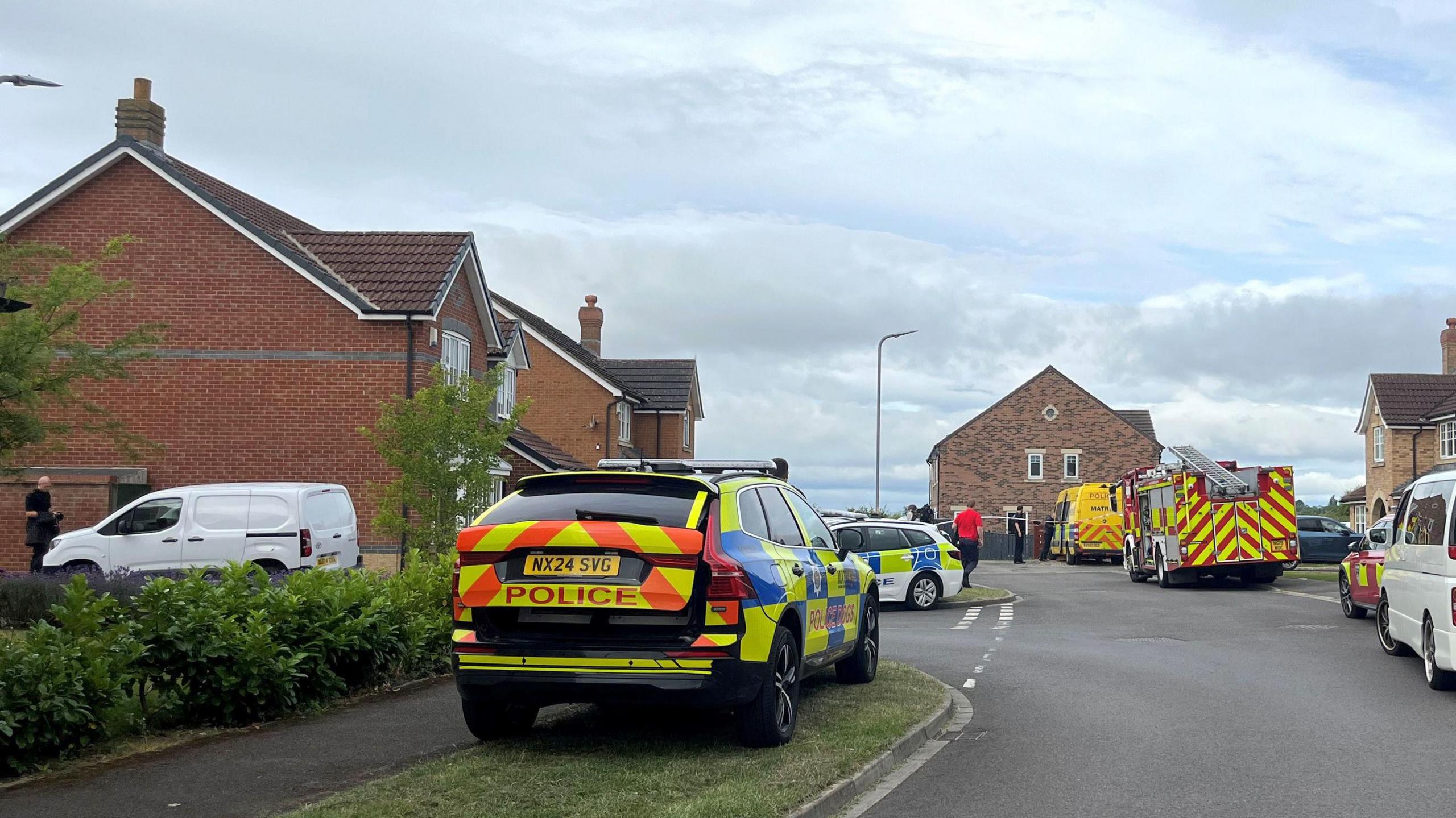A street view of Ramsey Gardens which has new-build homes lining it is covered in police cars and fire engines.