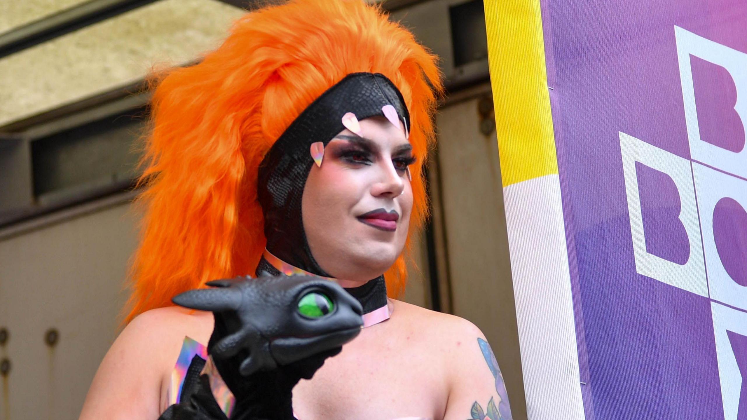 Someone is wearing a large orange wig and is holding a puppet.