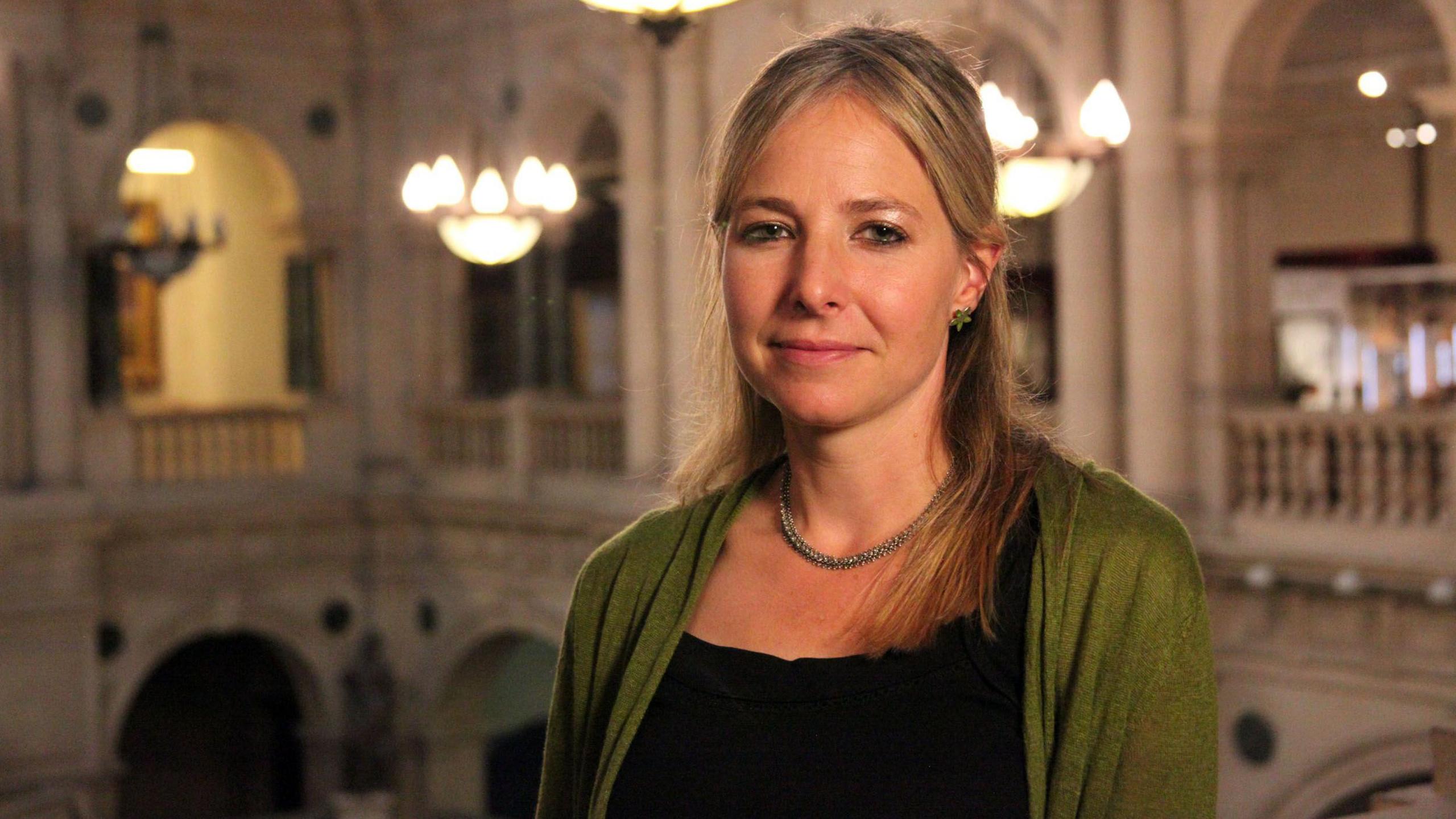 Professor Alice Roberts inside Bristol Museum, wearing a green and black top and looking at the camera