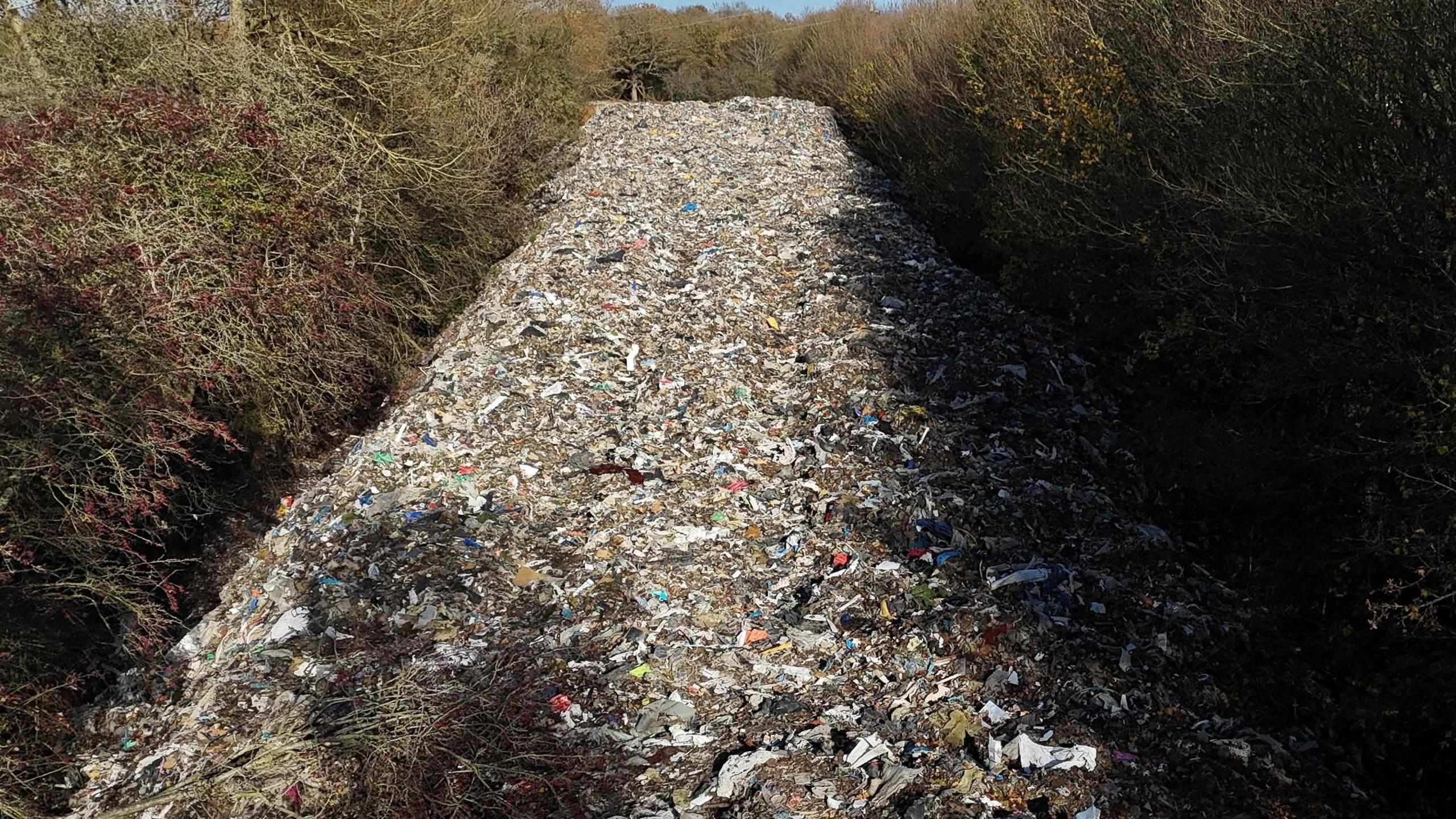 A huge pile of rubbish stretching into the distance with trees on either side