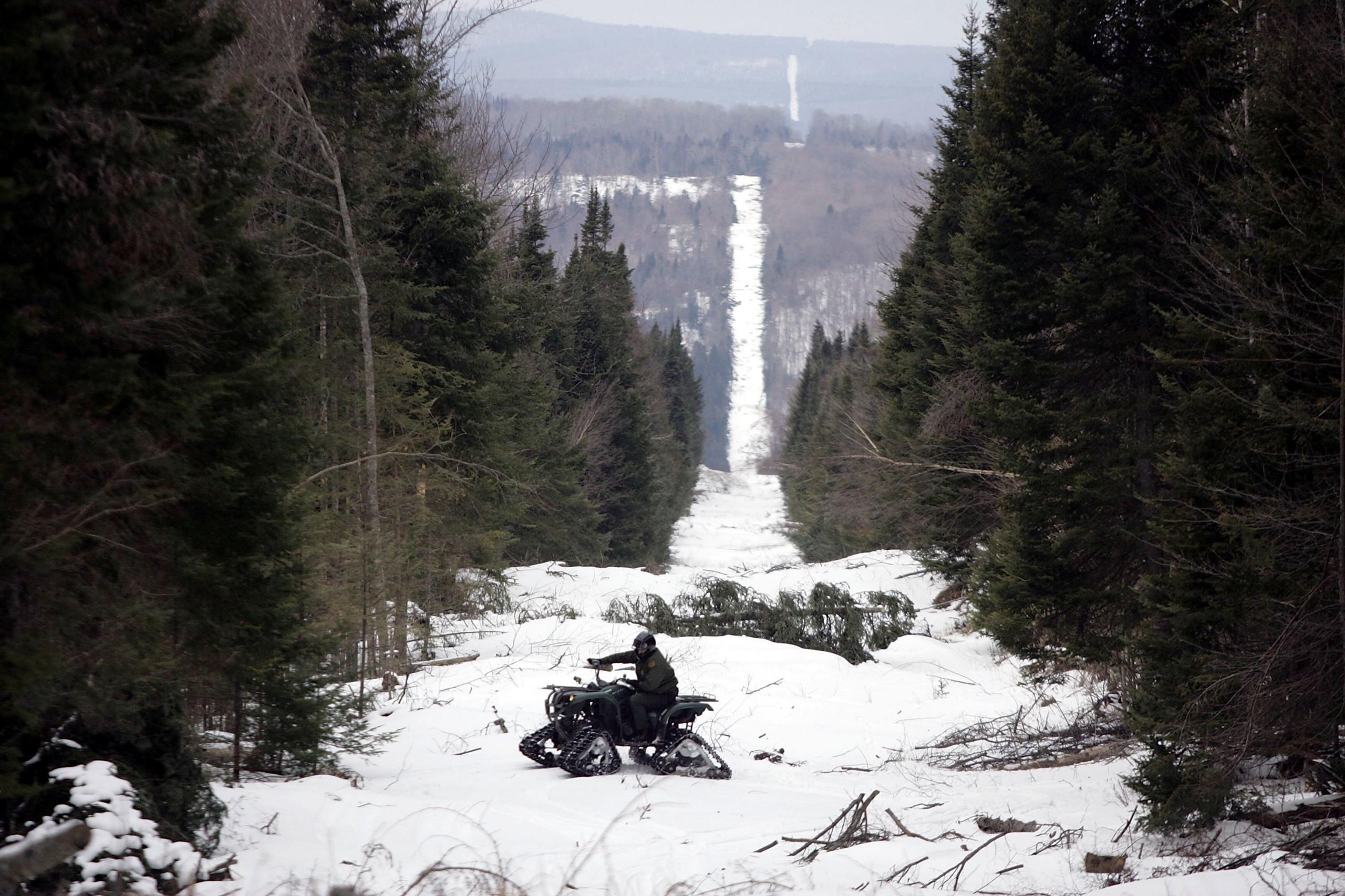 U.S. Border Patrol Agent Andrew Mayer rides a ATV as he looks for signs of illegal entry along the boundary marker cut into the forest marking the line between Canadian territory on the right and the United States March 23, 2006 near Beecher Falls, Vermont.