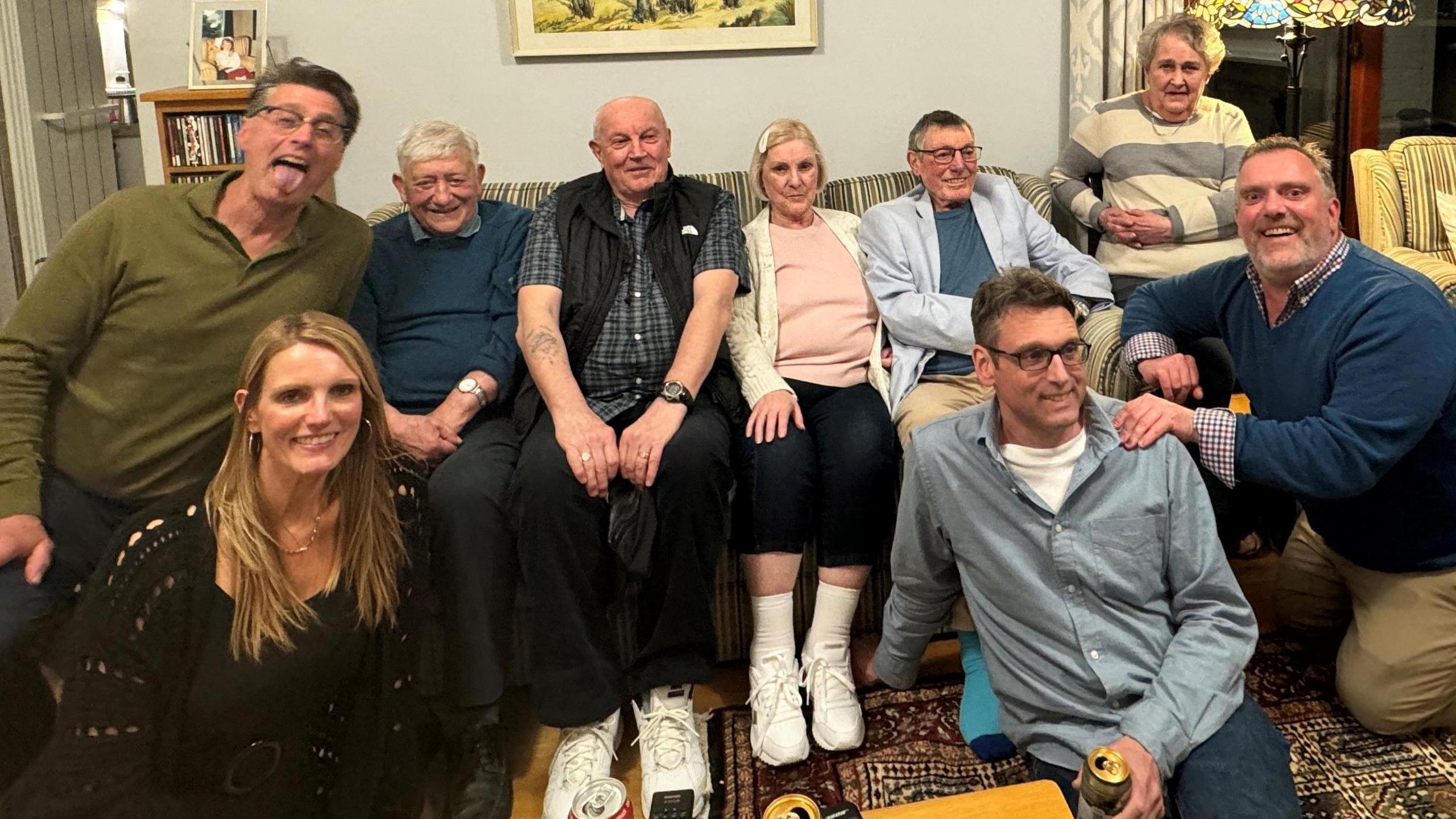 Six people sitting on a sofa in a room and three people sitting on the floor in front of the sofa