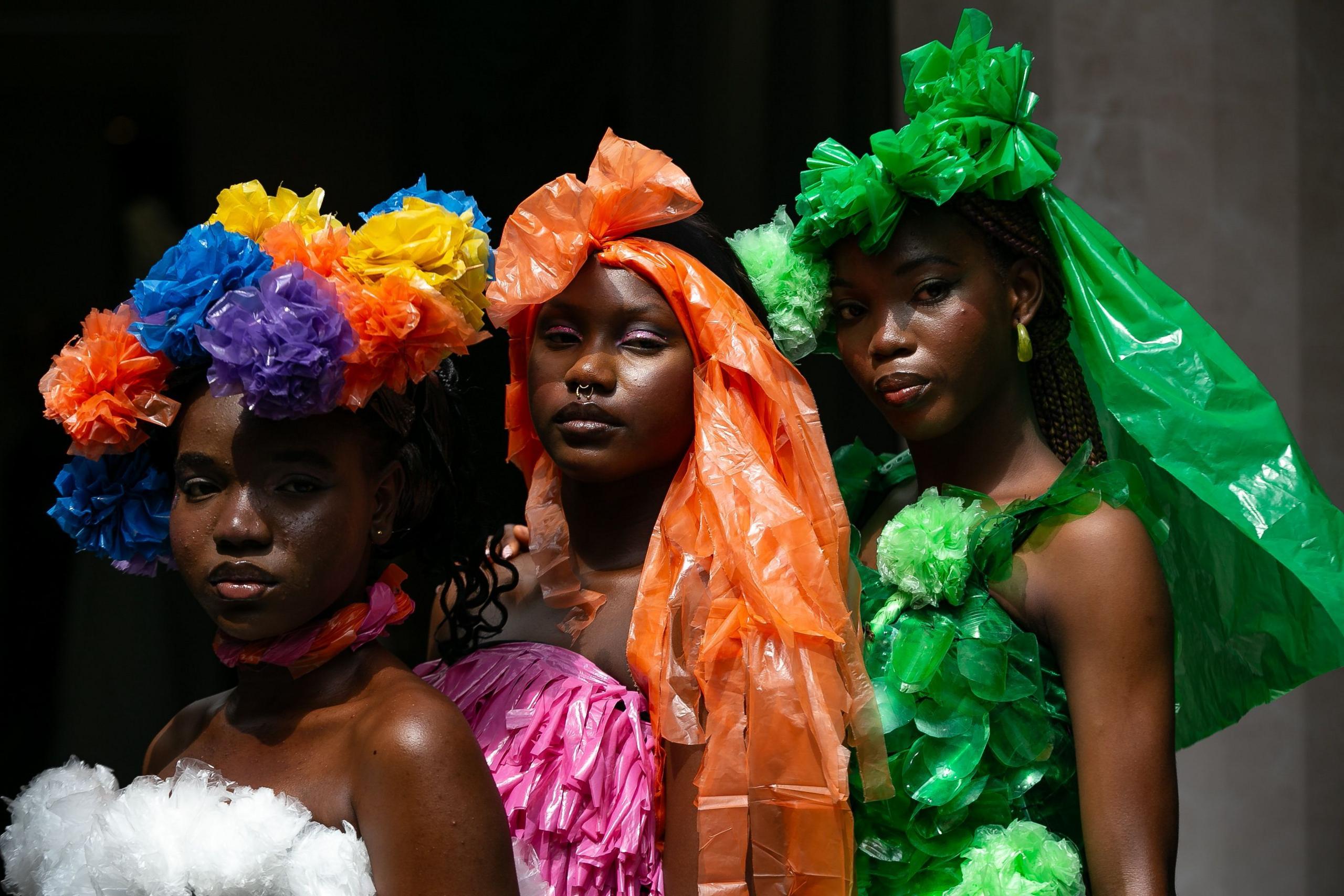 Models wear outfits made of plastic bags in bright colours.