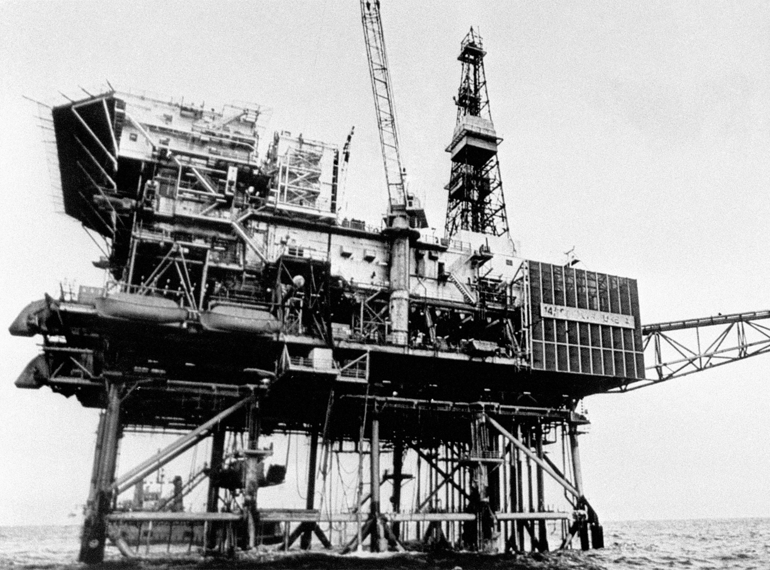 Piper Alpha, a huge oil production platform, stands out of the North Sea. The whole structure is covered in metal coping and fabricated panels. A tall oil derrick dominates the centre of the structure and the sea is quite calm.