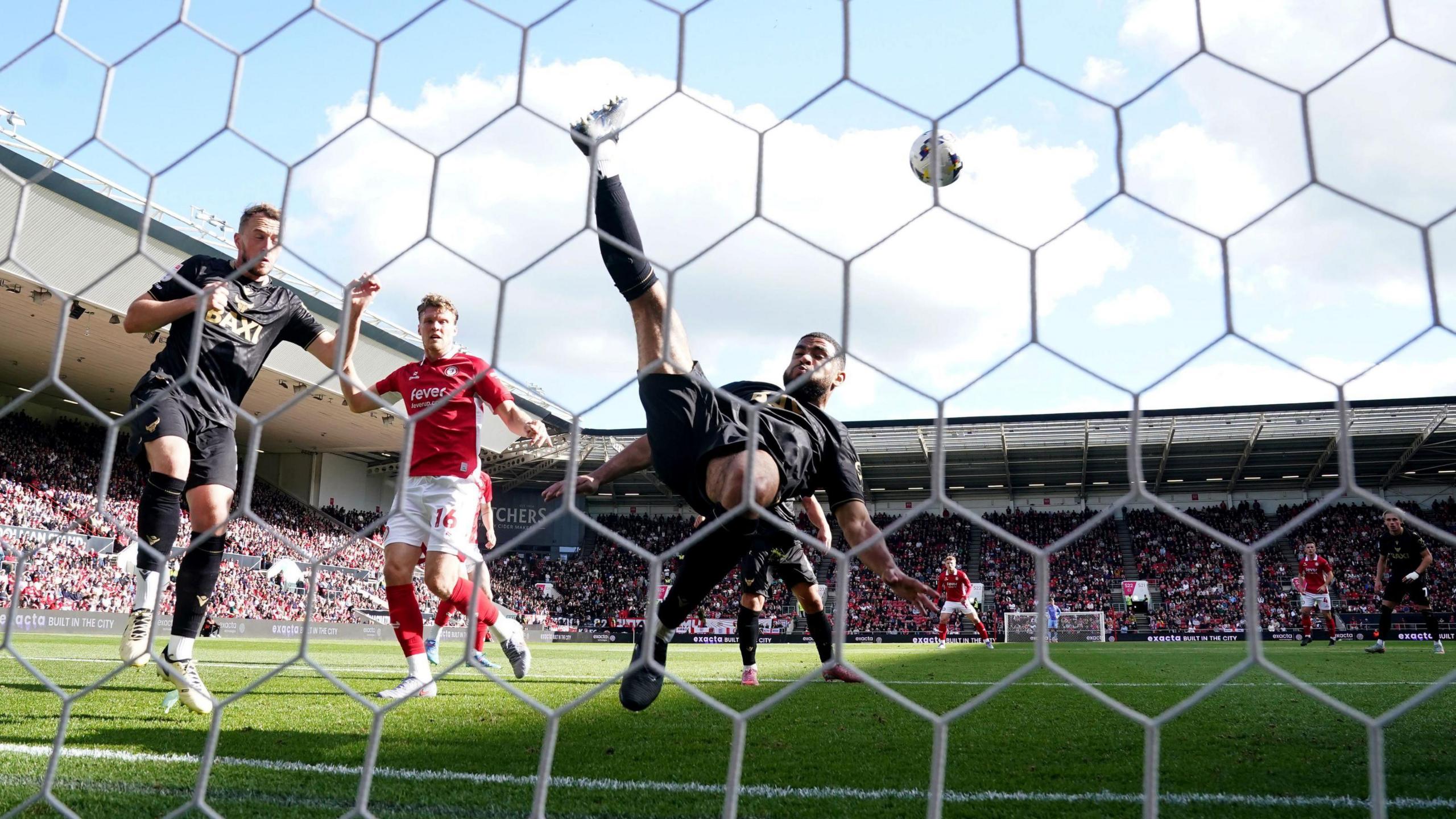 Oxford United's Brodie Spencer is seen in mid air as he clears the ball from his own goal line with an overhead kick during the match with Bristol City at Ashton Gate. In the background the stands of the stadium are seen to be full