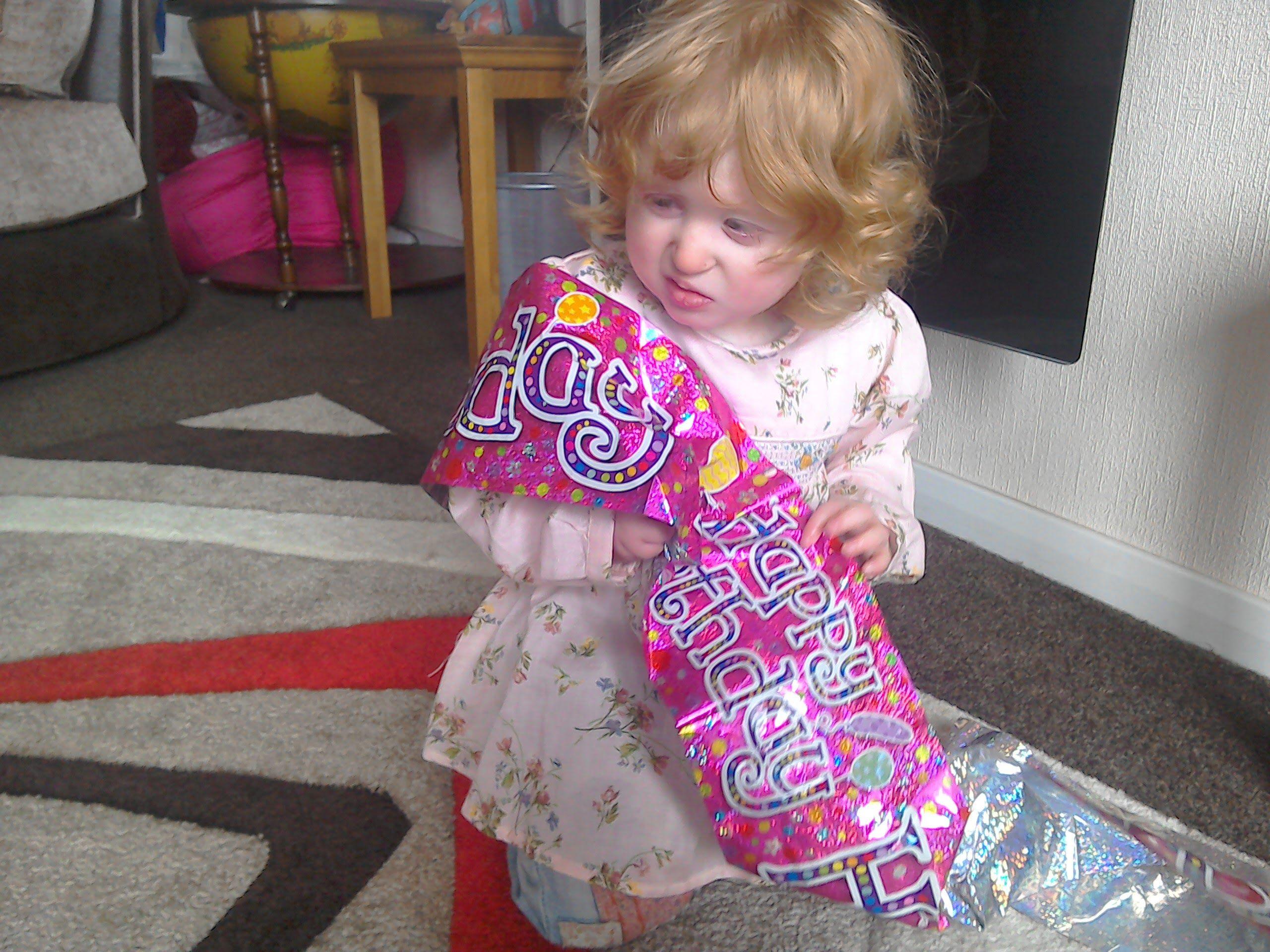 Young Jadyi with curly hair and a pink floral dress holding a vibrant pink banner than says Happy Birthday