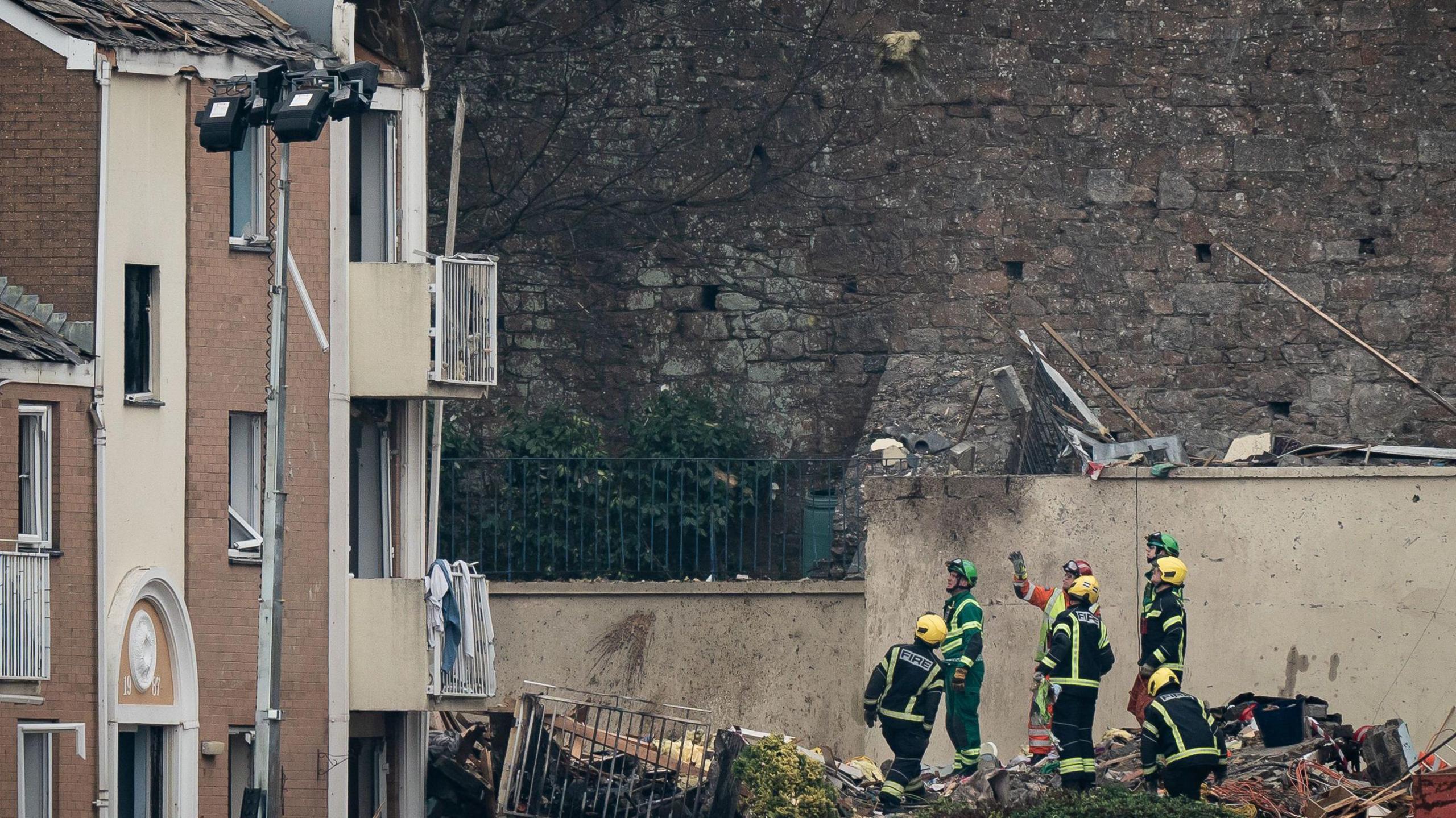Four firefighters, two paramedics and an engineer examine the site of an explosion in Haut du Mont, St Helier, Jersey. They are stood on a pile of rubble.