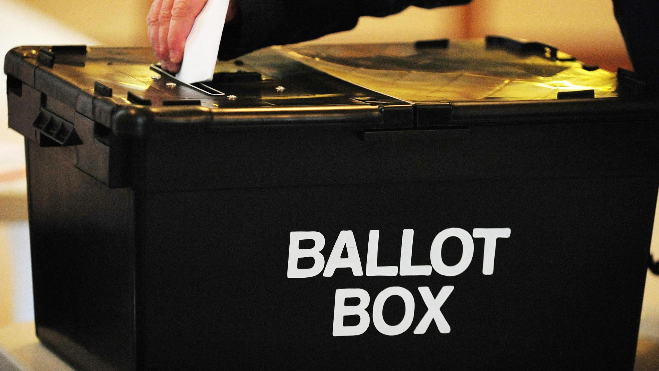 The hand of a voter wearing black places a ballot paper in the ballot box at a polling station.