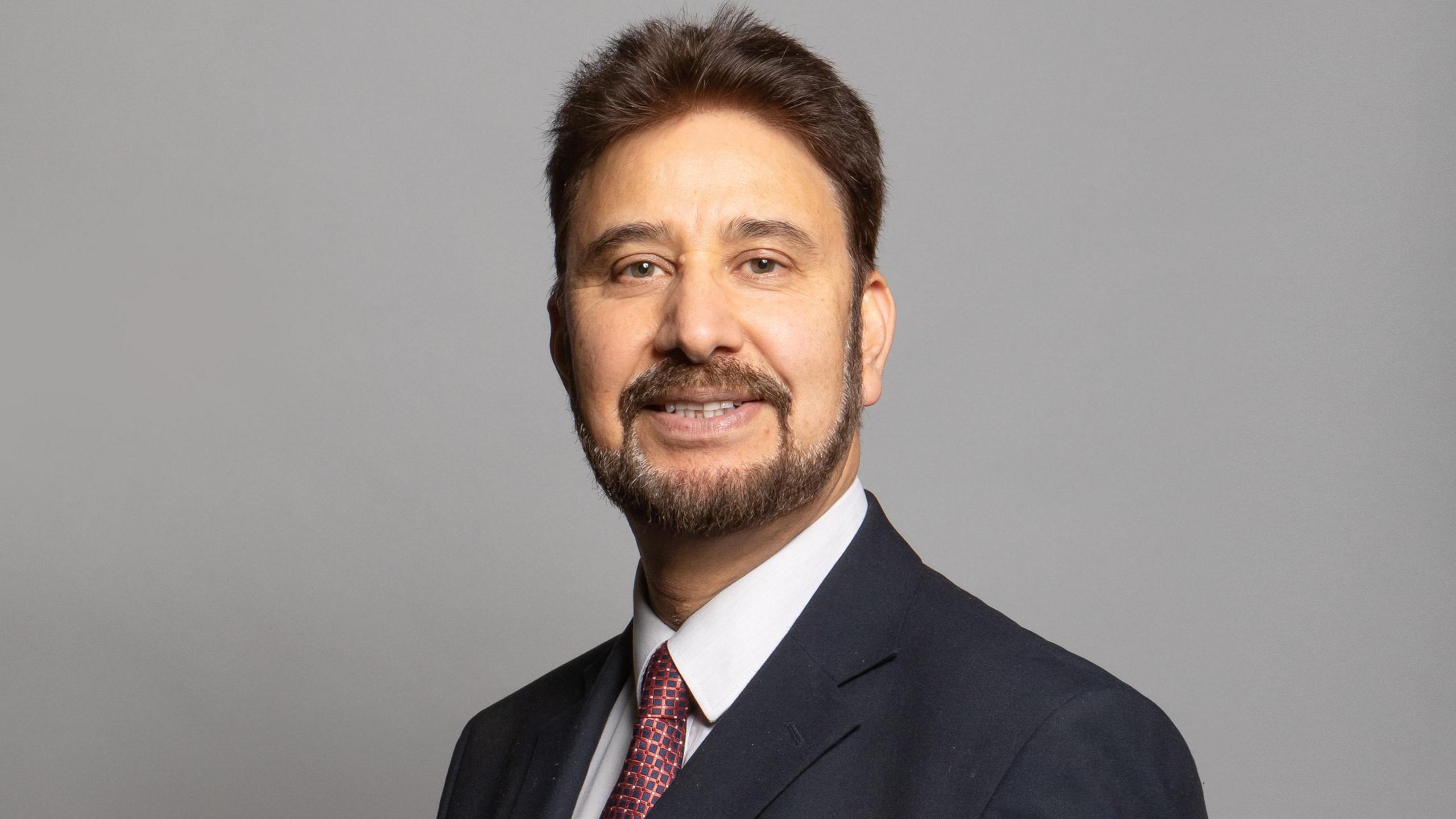 Official portrait of Afzal Khan, a middle aged man wearing a blazer and checked red tie