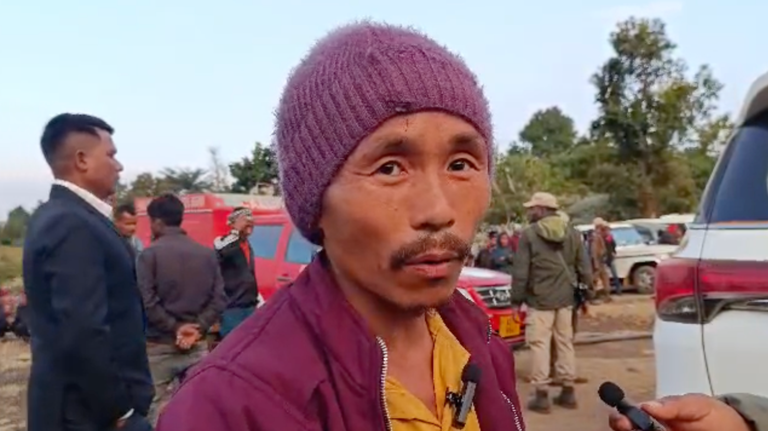 A photo of Ravi Rai, wearing a red hat, a red jacket and a yellow T-shirt, speaking to a reporter. He is among the miners that successfully escaped when an illegal mine was flooded in India's Assam state.