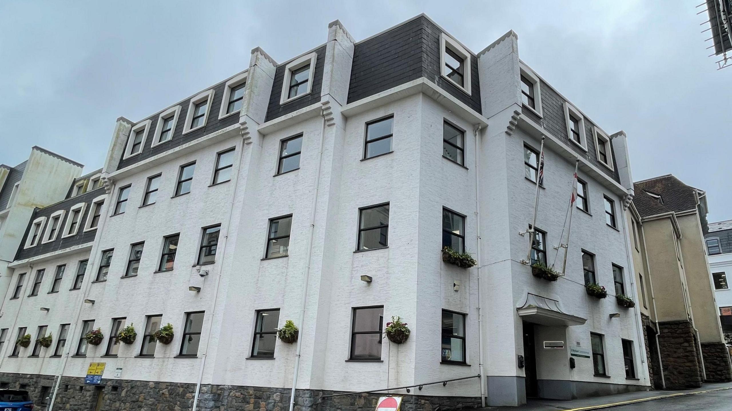 A four-storey white building on a corner block under a cloudy sky.