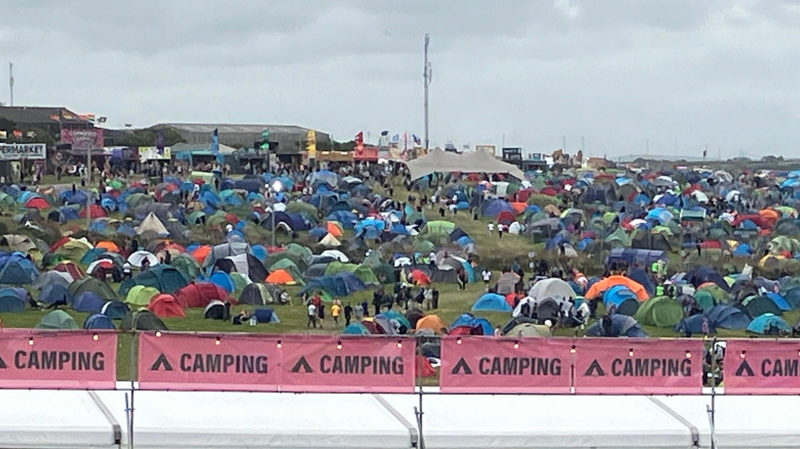 A sloping field is covered with spherical and triangular tents in multi-colours.