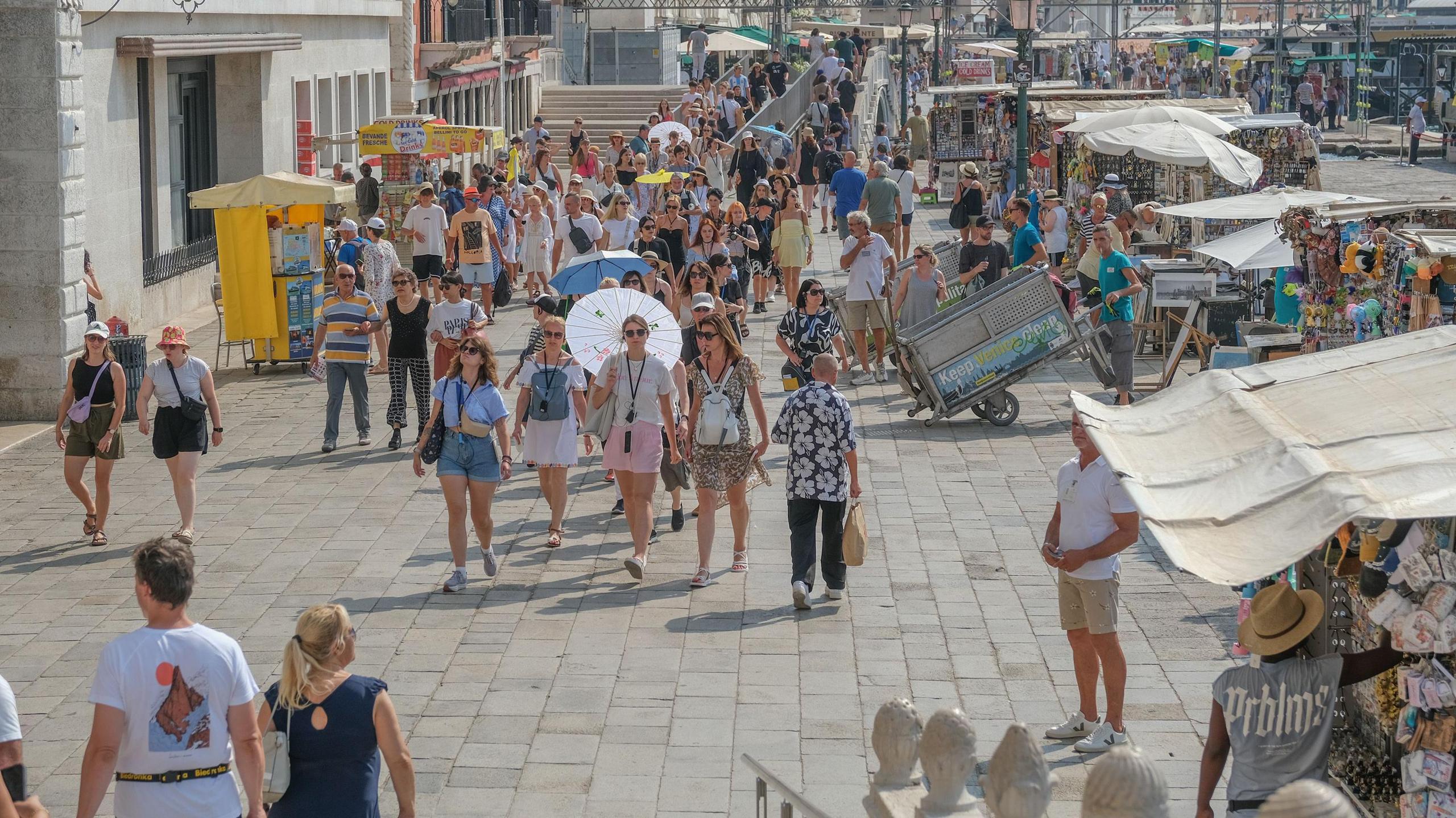 Crowds of people walking through St Mark's Square in Venice, past some stalls selling souvenirs. 