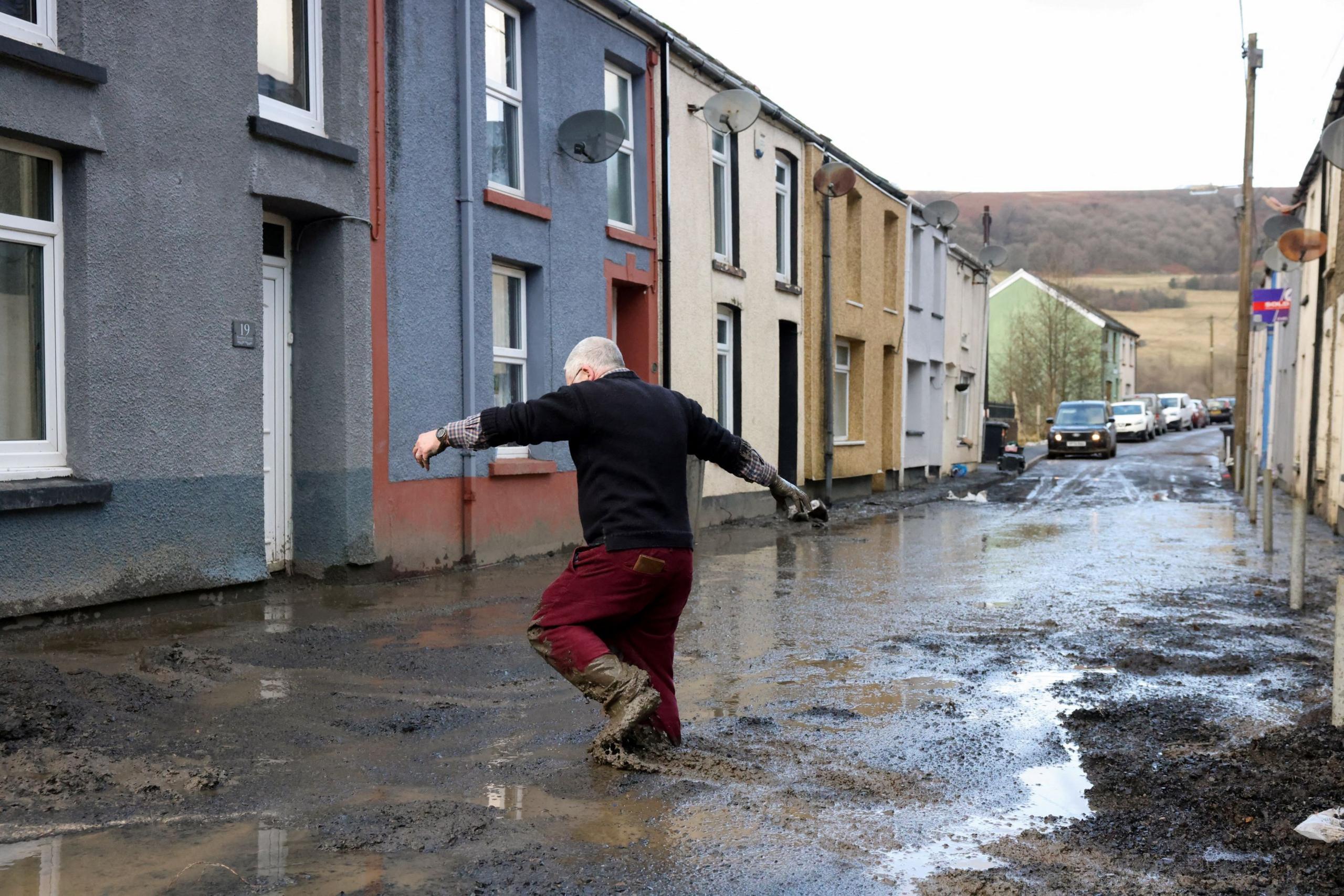 A local resident tries to wade through mud at the site of a landslide in Cwmtillery, South Wales. He is up to his knees in mud.