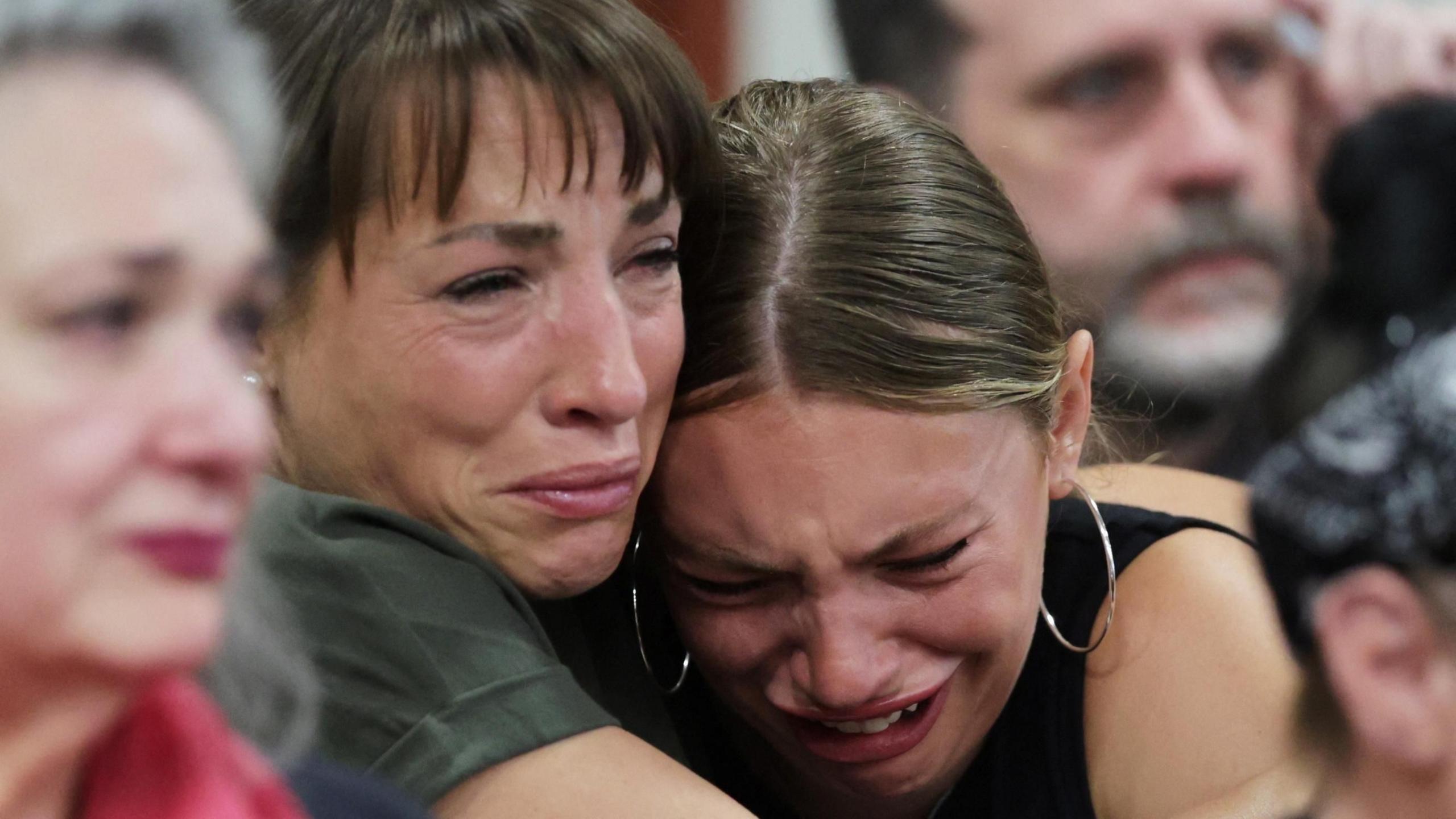 Dylan Mortensen cries into the shoulder of another woman who is also crying