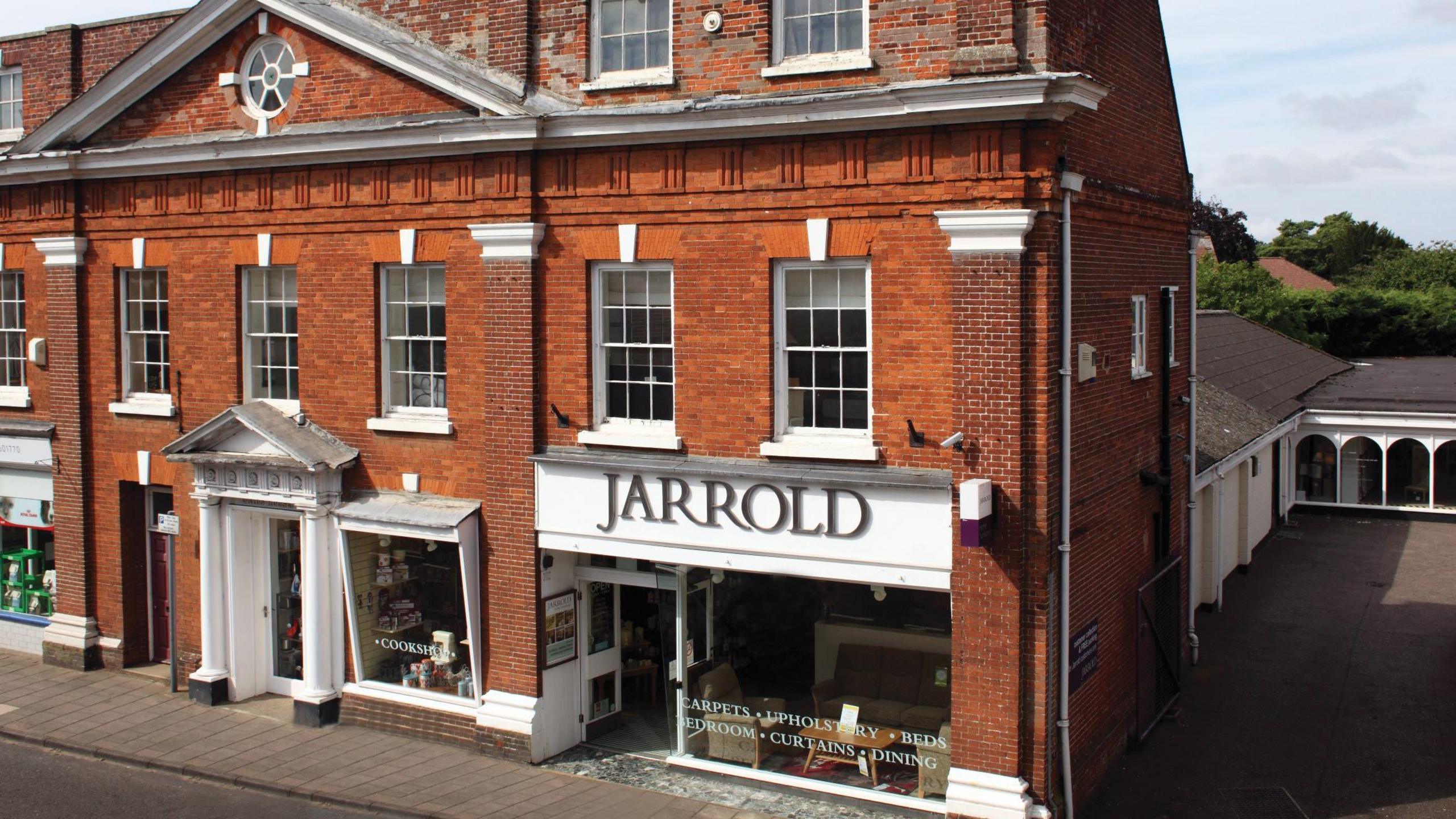 A large red-bricked building on a High Street, with a glass-fronted shop front with a sign reading "Jarrold" above it. 