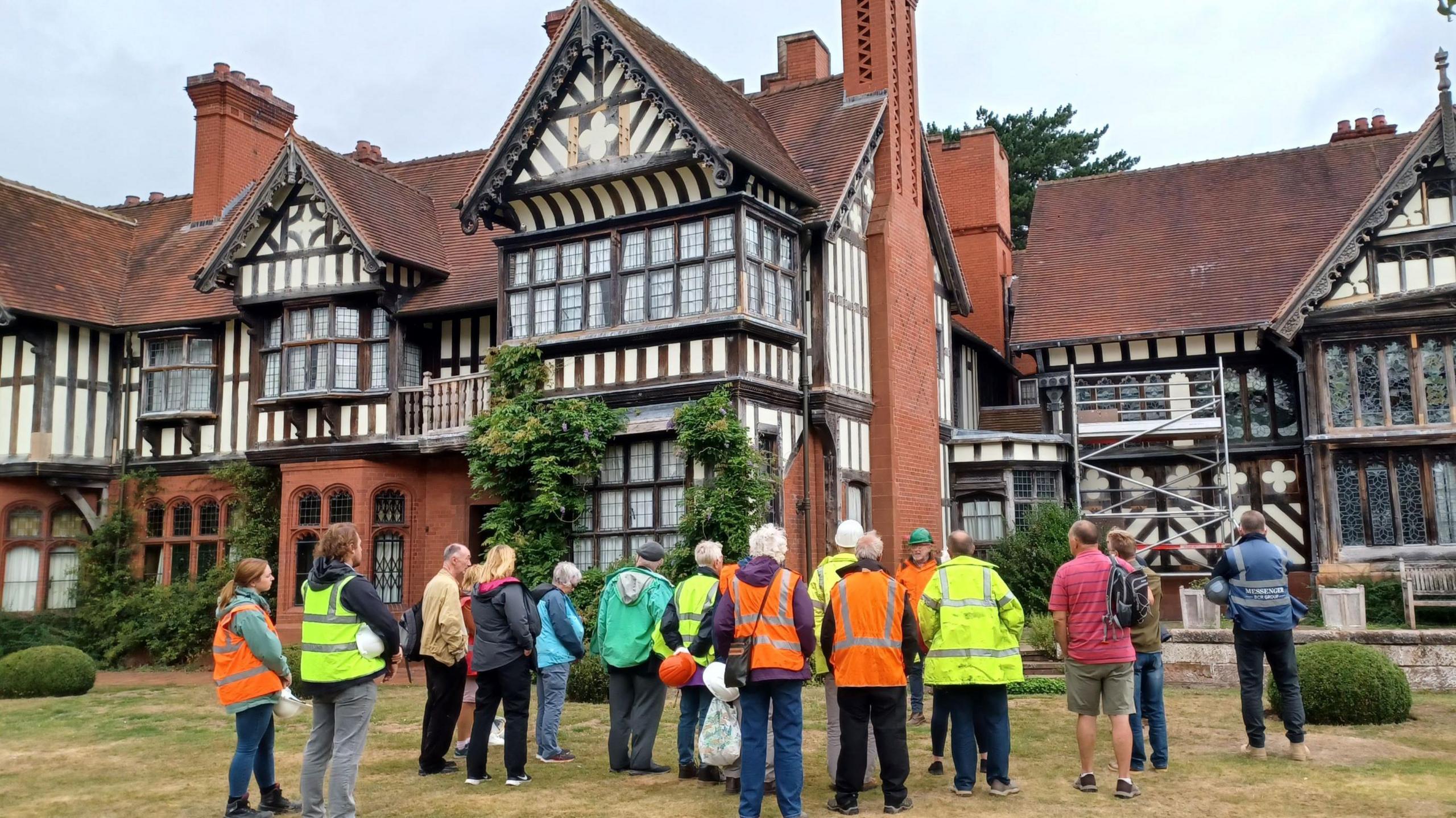 Exterior view of Wightwick Manor, a historic red-brick building with a prominent timbered upper storey and numerous windows, set against a backdrop of greenery.
