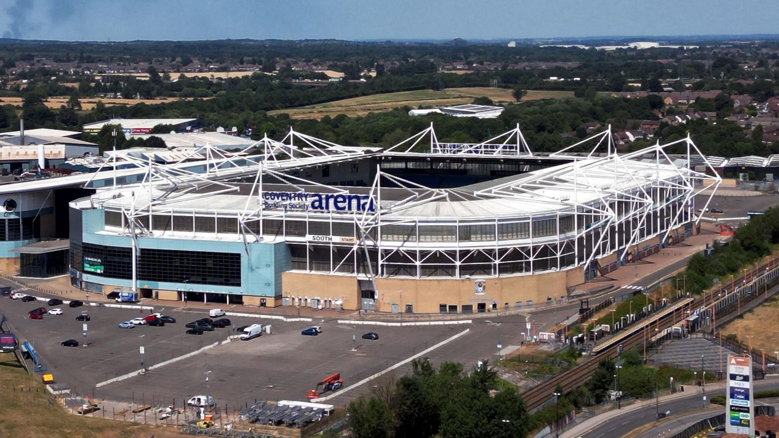 Aerial view of the Coventry Building Society Arena with the signage for the stadium visible as well as the car park surrounding the bowl-shaped structure with white supporting beams.