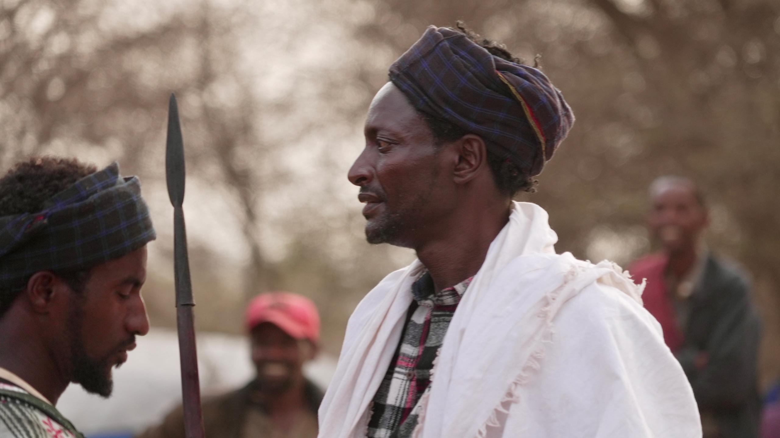 A man in a white robe carries a spear.