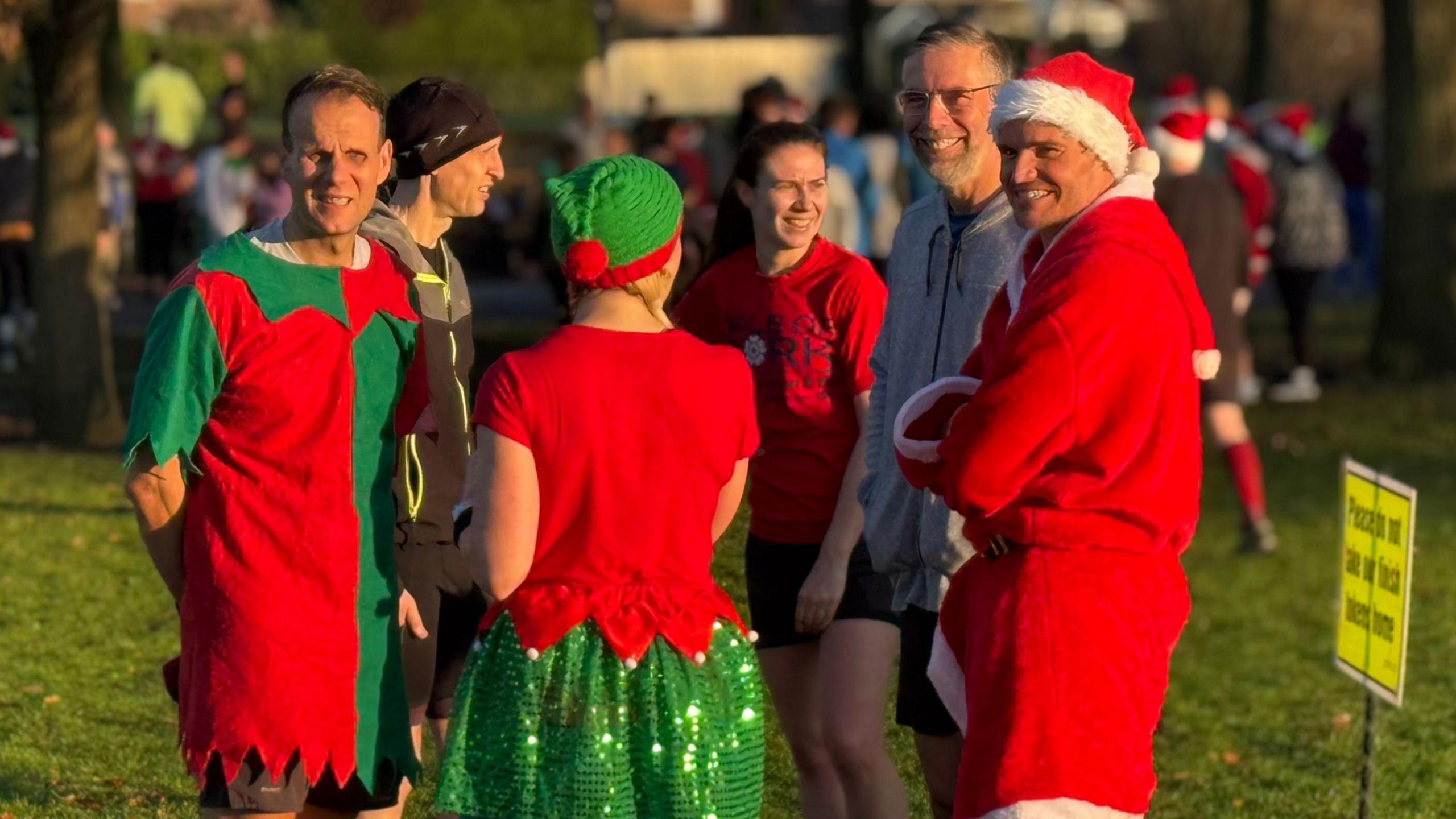 A group of people stood in a park, some with their back to the camera. They are wearing festive outfits.