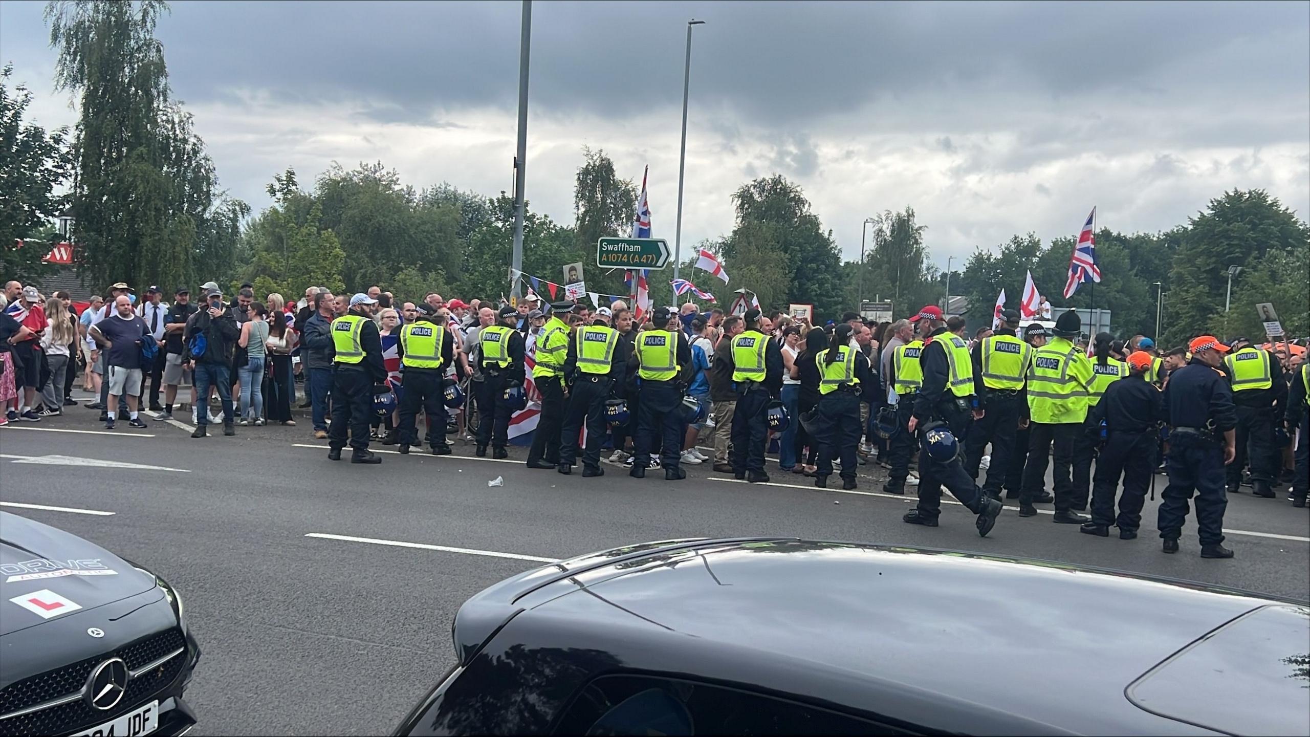 People waving flags and a line of police officers standing in front of them.