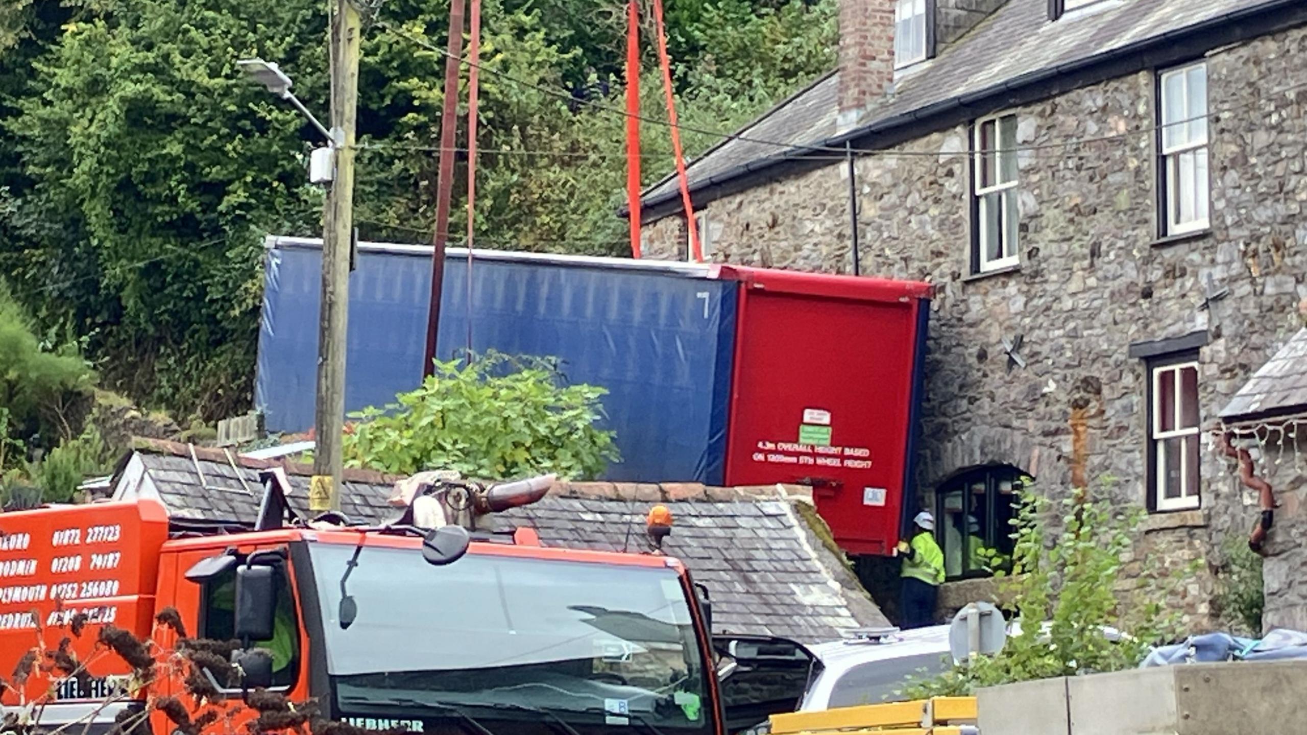 A red and white lorry trailer with straps around it and part of the crane in the foreground