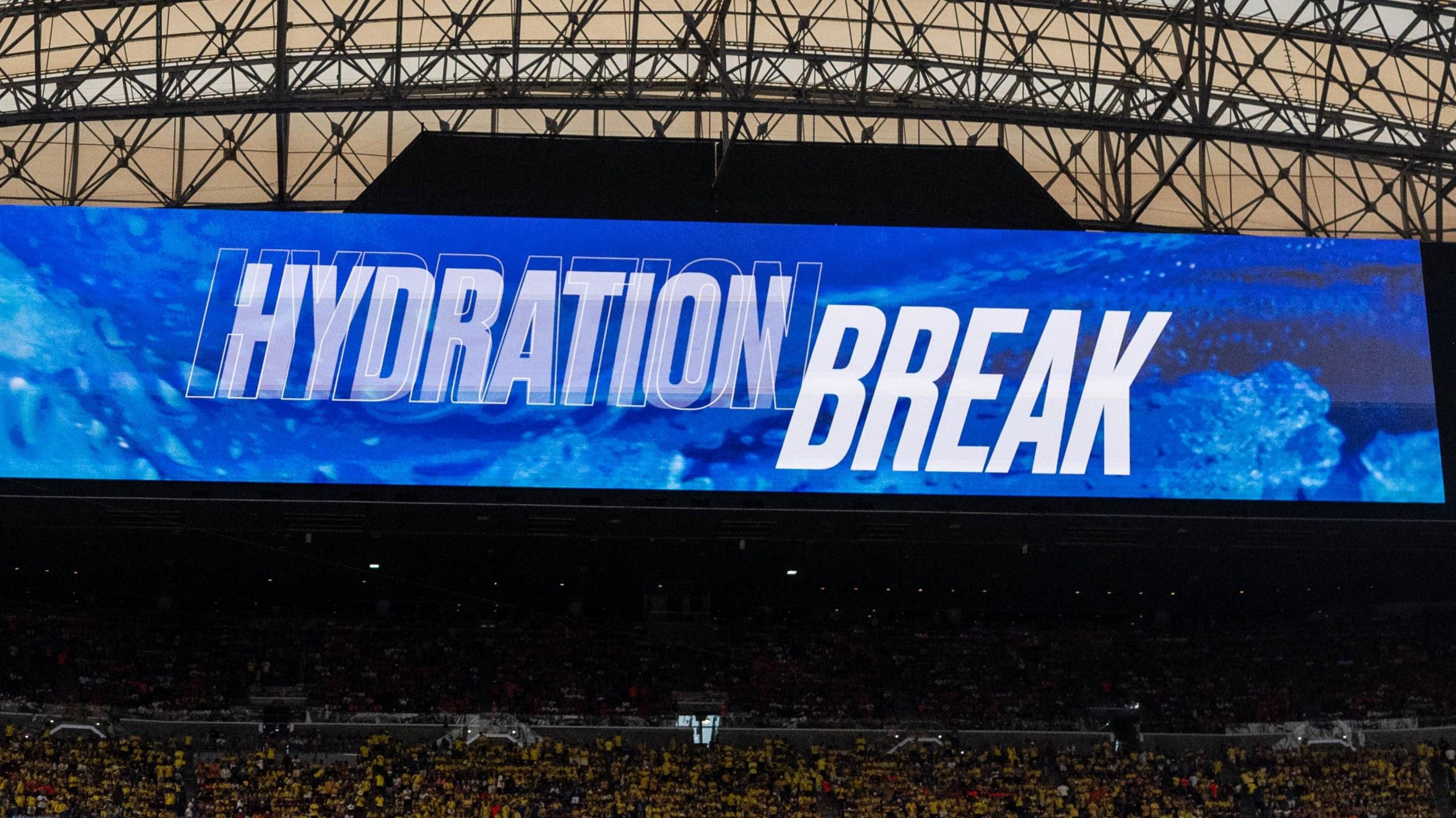 Television screen inside a stadium shows the words "hydration break" at the World Cup