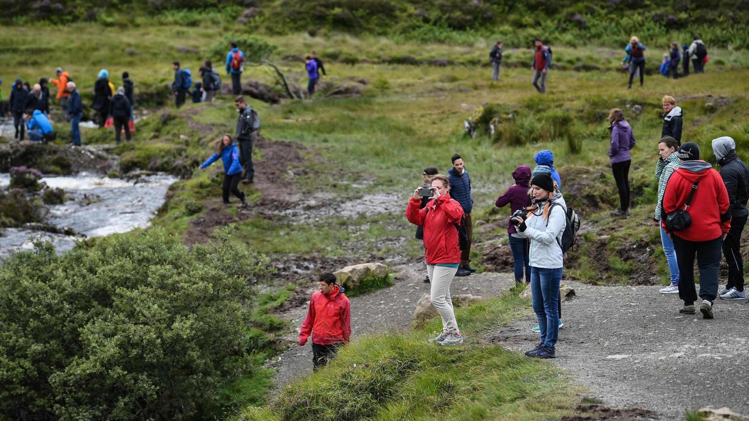A picture taken on Skye in 2017 showing tourists wearing brightly coloured jackets and fleeces exploring a glen with a river running through it.