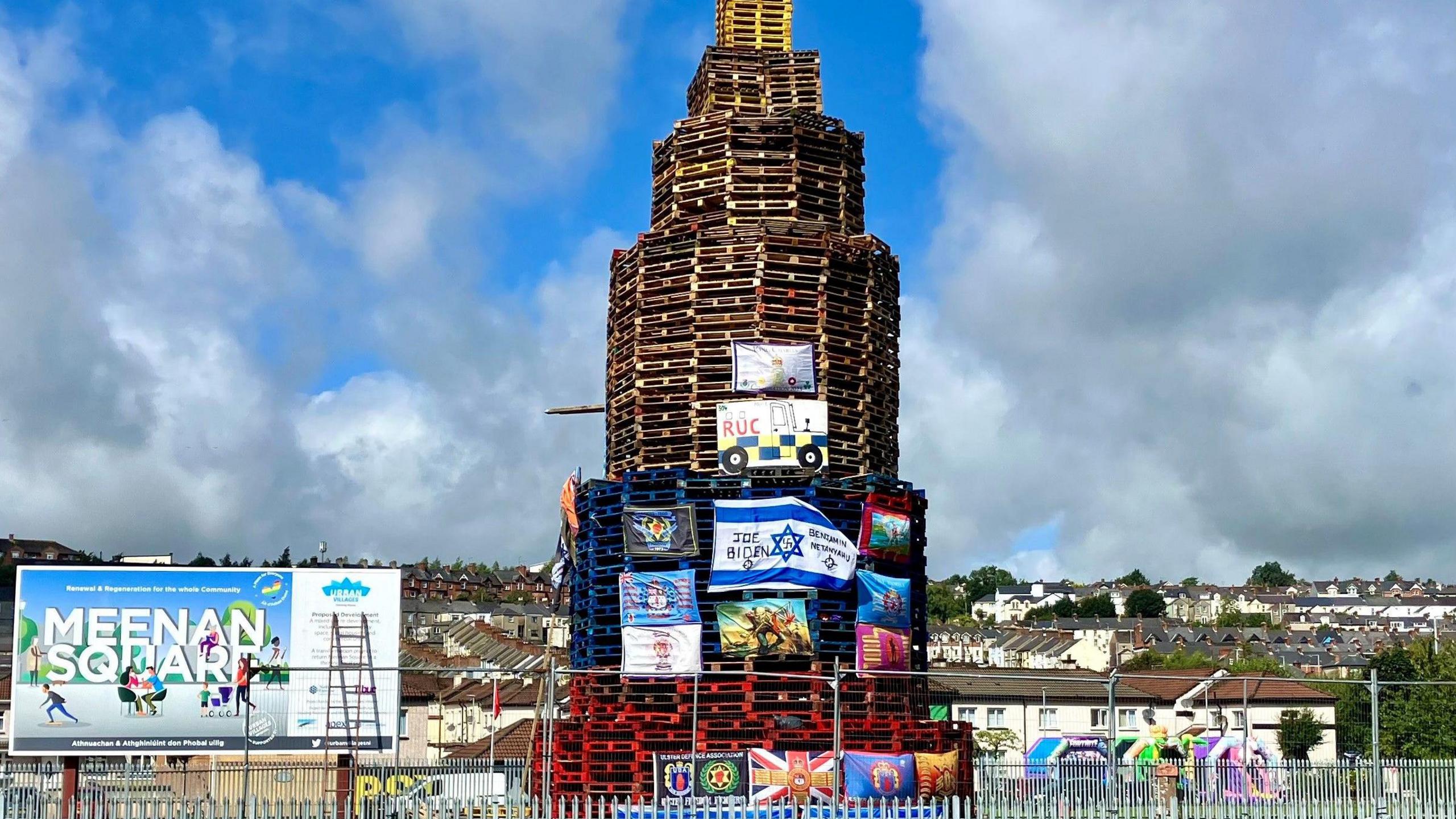 A bonfire in Derry's bogside made from pallets and covered in flags including unionist items and the flag of Israel