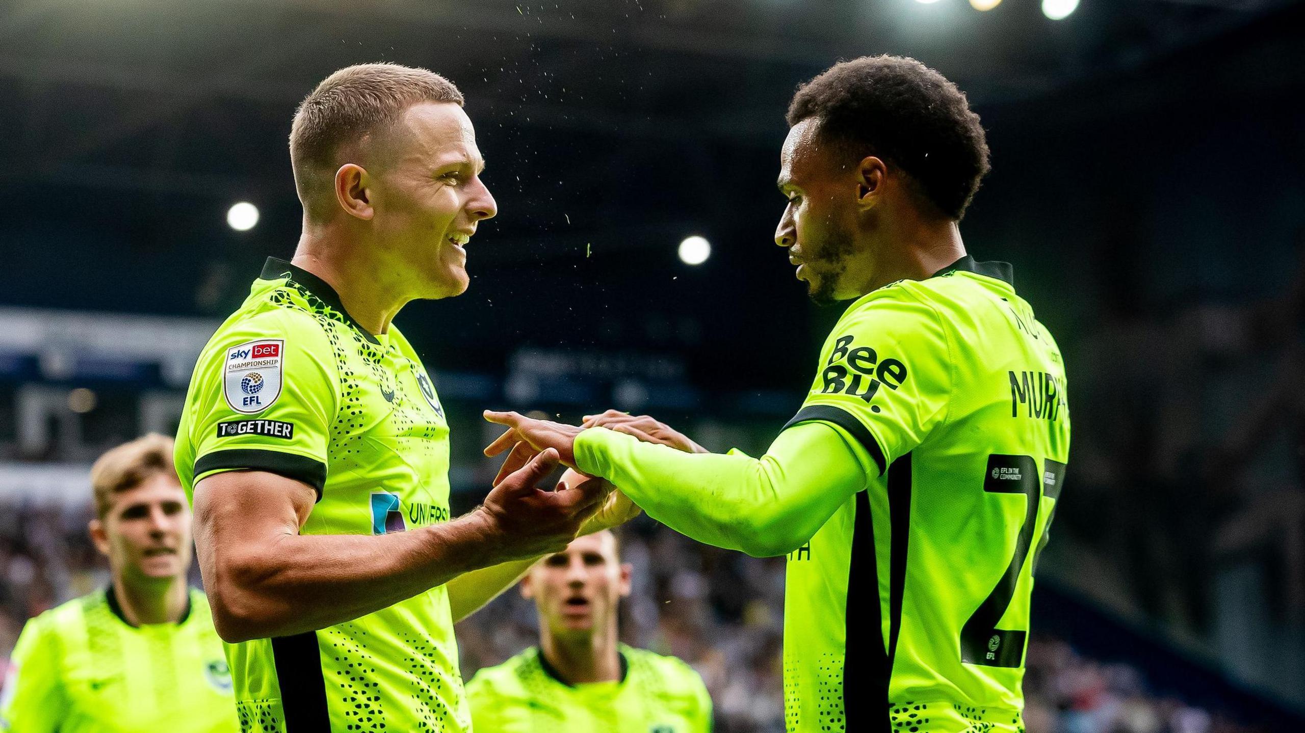 Colby Bishop (left) clasps hands with team-mate Josh Murphy and faces him smiling in celebration of a goal
