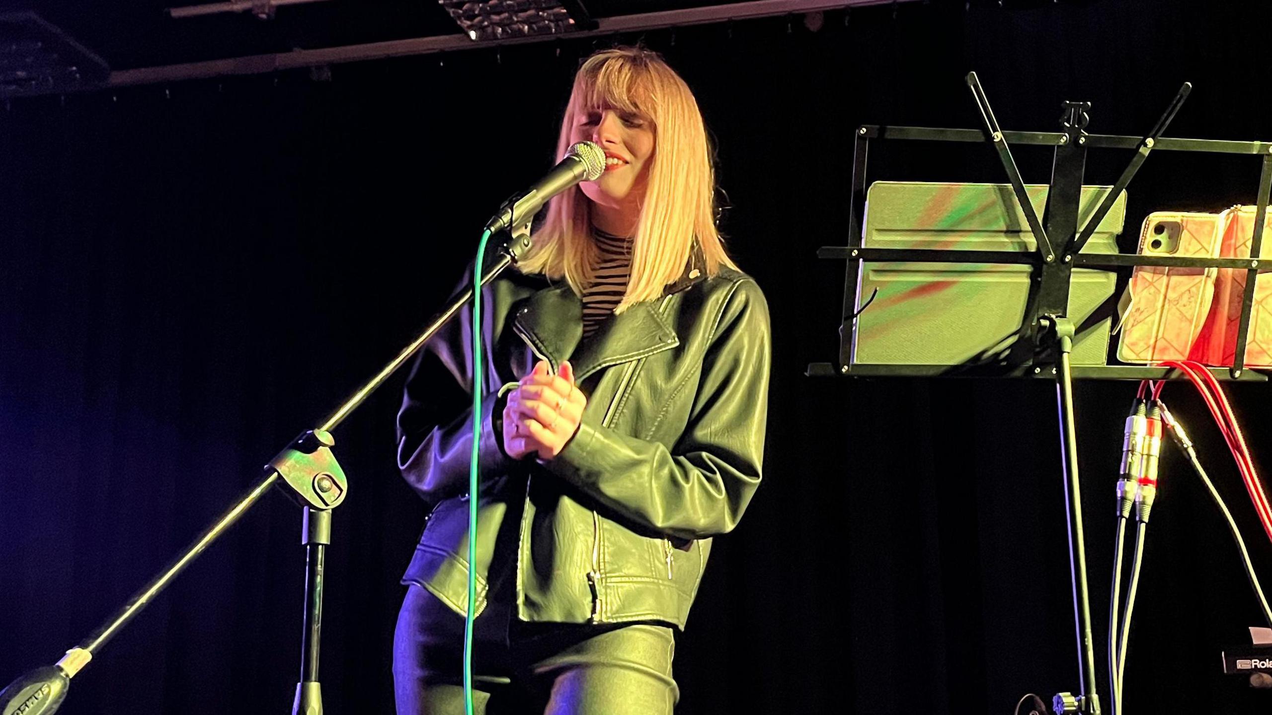 Jasmine Rose sings into a microphone on stage, with her eyes closed.