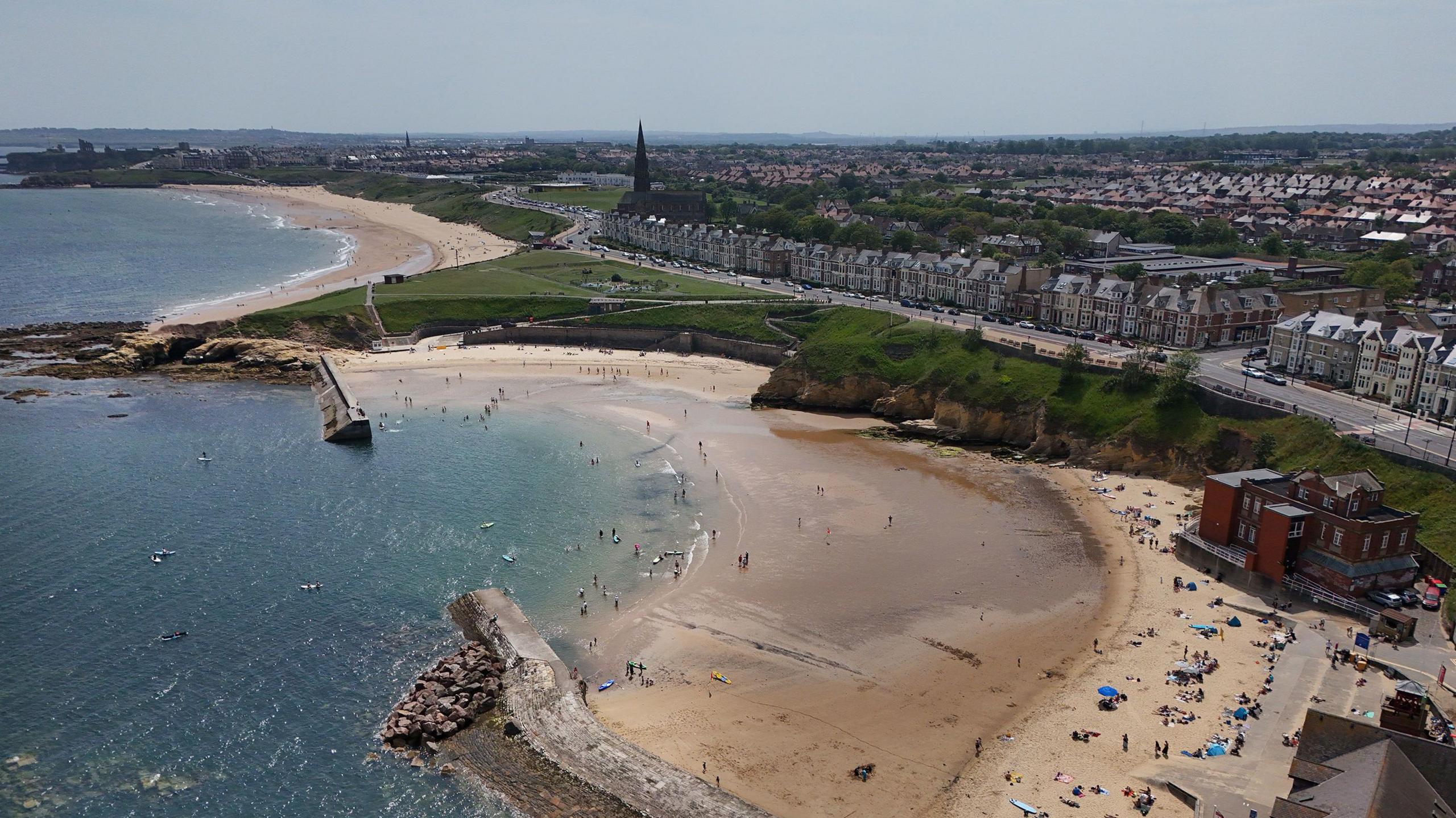 An aerial shot of a busy beach and the sea, with a town in the background