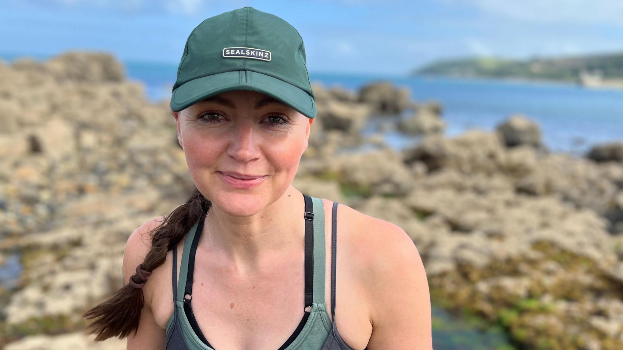 Make a Difference Cornwall winner Katie Maggs on the coast with rockpools behind. She has a green hat and green top on.