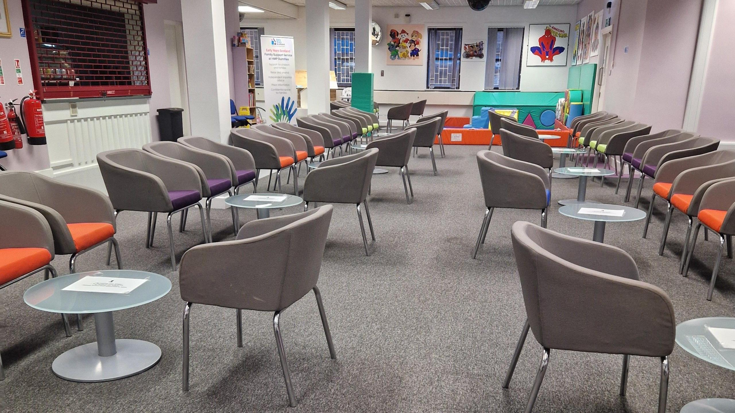 A seating area with tables and chairs. The walls are lilac and the chairs are grey.