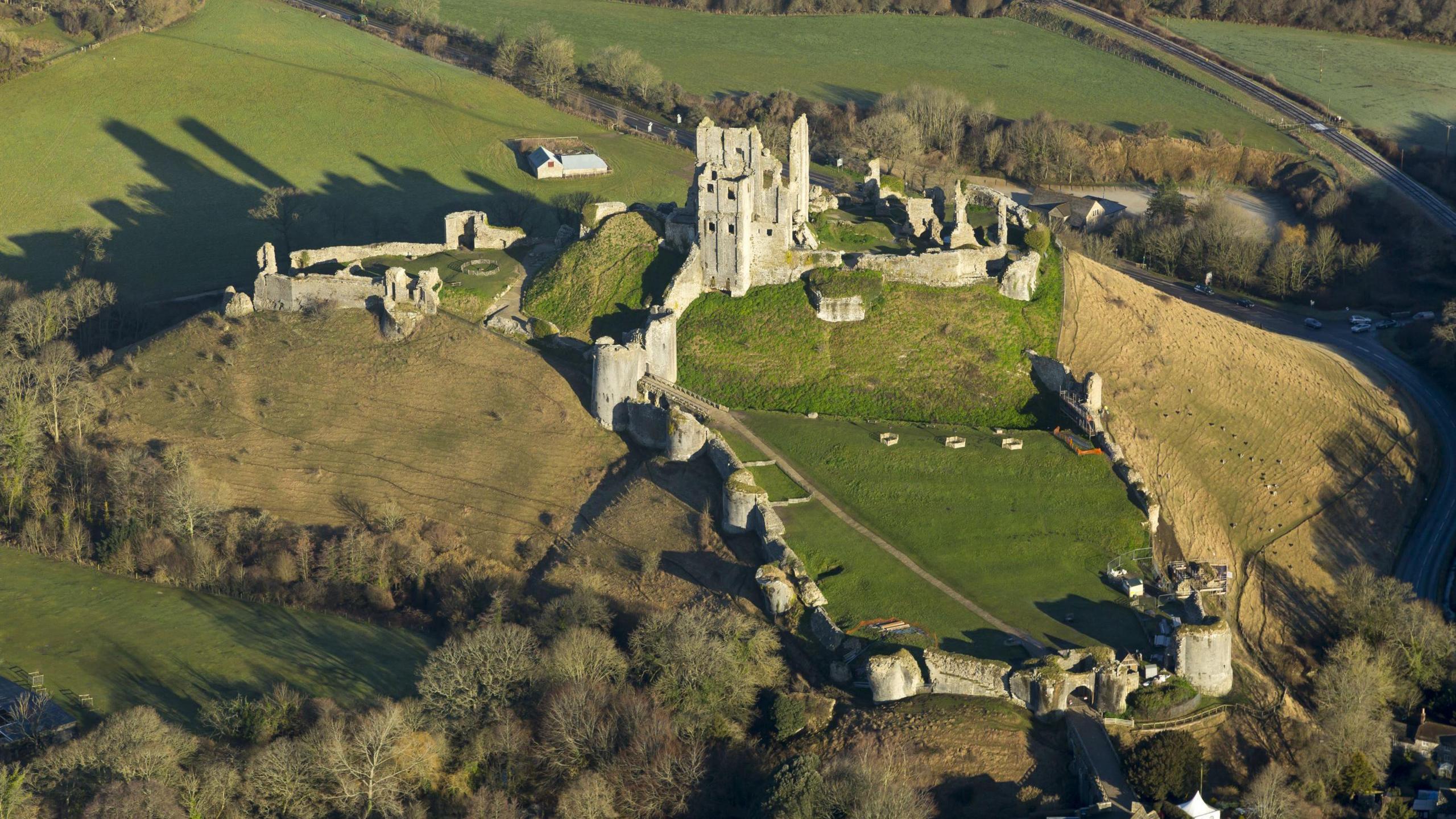 An aerial image of Corfe Castle which has a main structure still stood atop of a hill and a wall spreading down the hill and around the countryside